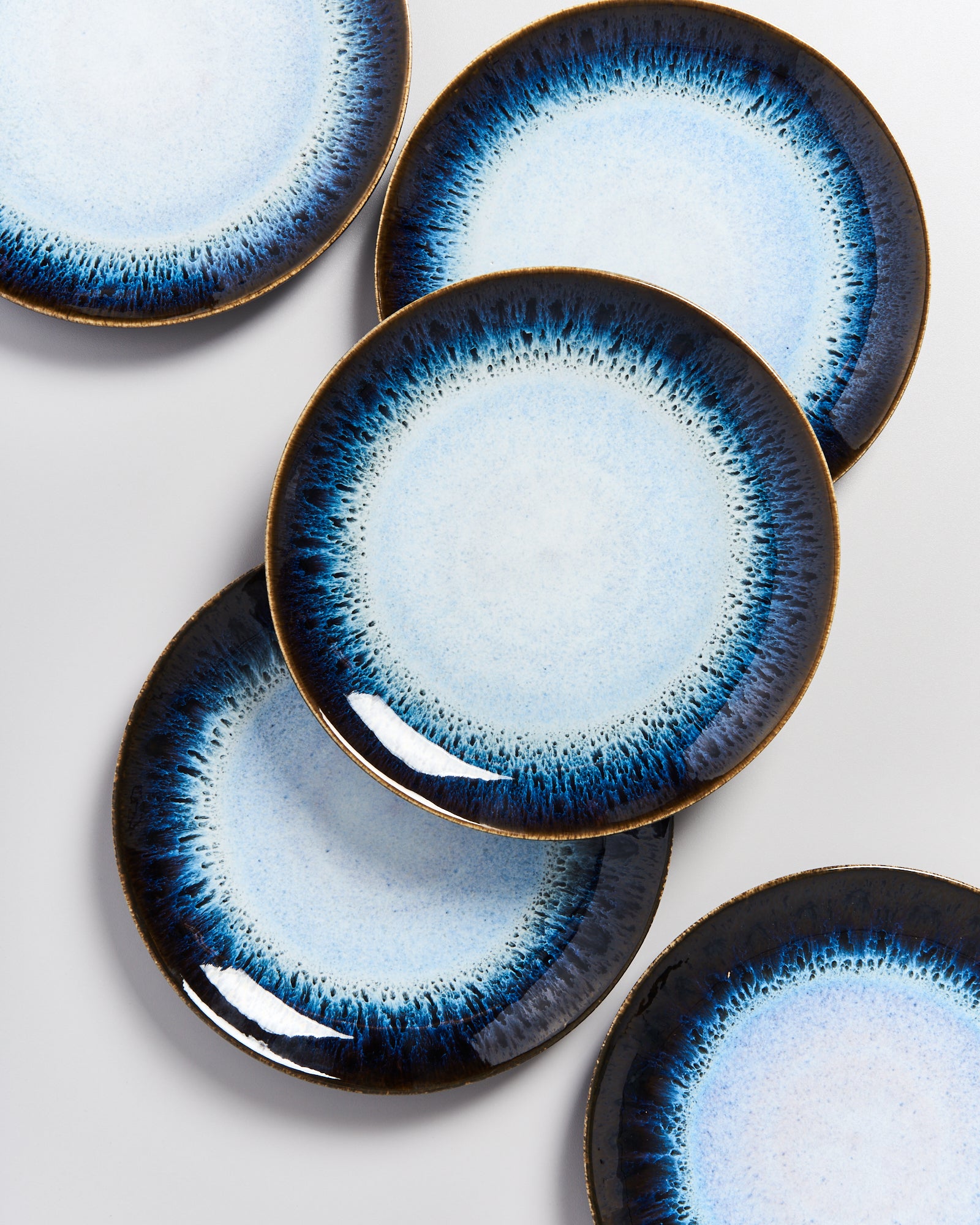 Fünf blaue und weiße Teller mit radialem Muster liegen überlappend auf einer hellen Fläche.