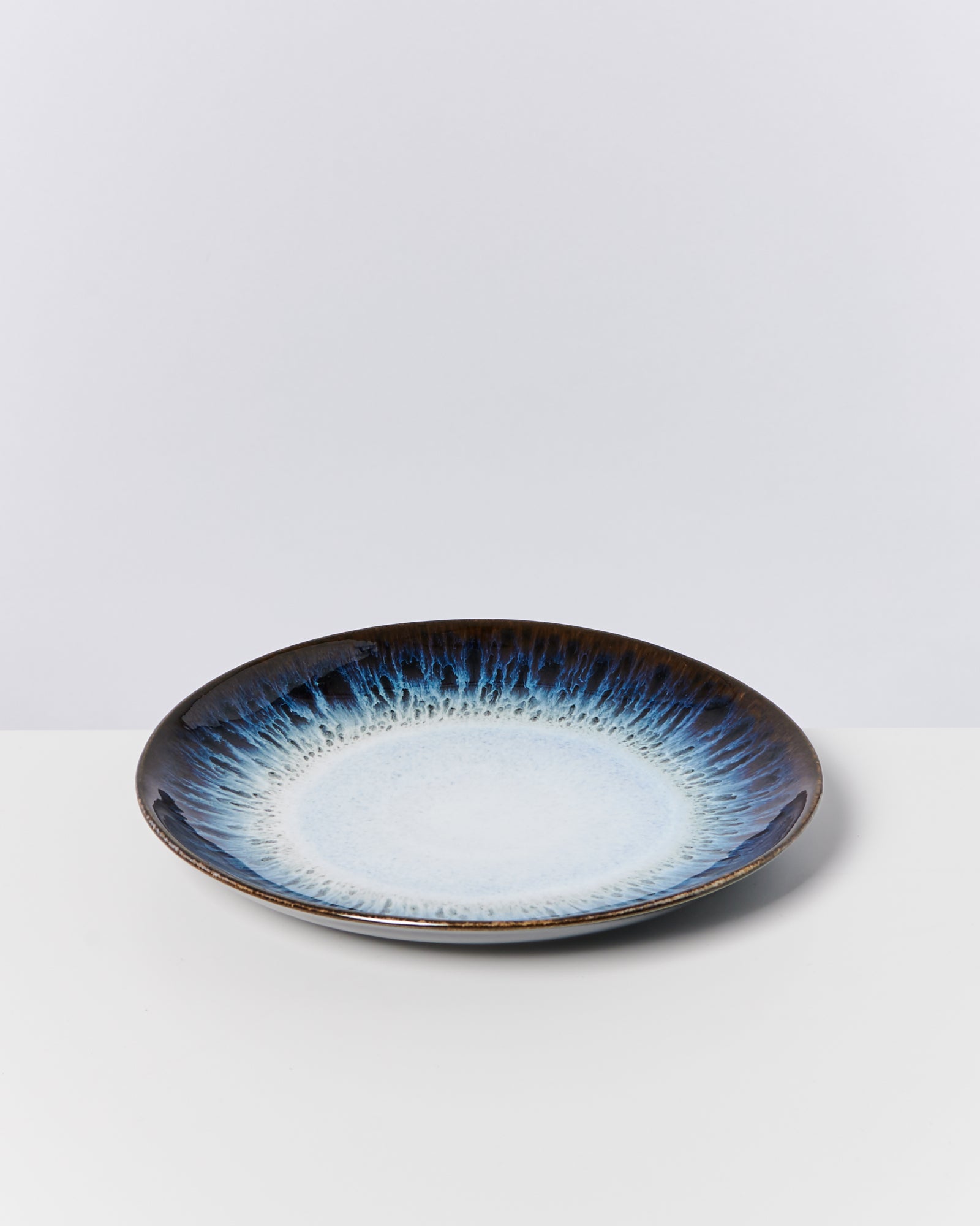 Keramikteller mit blau-weißer Glasur, die in einem ombre Verlauf von der Mitte zur Kante verläuft, auf weißem Hintergrund.