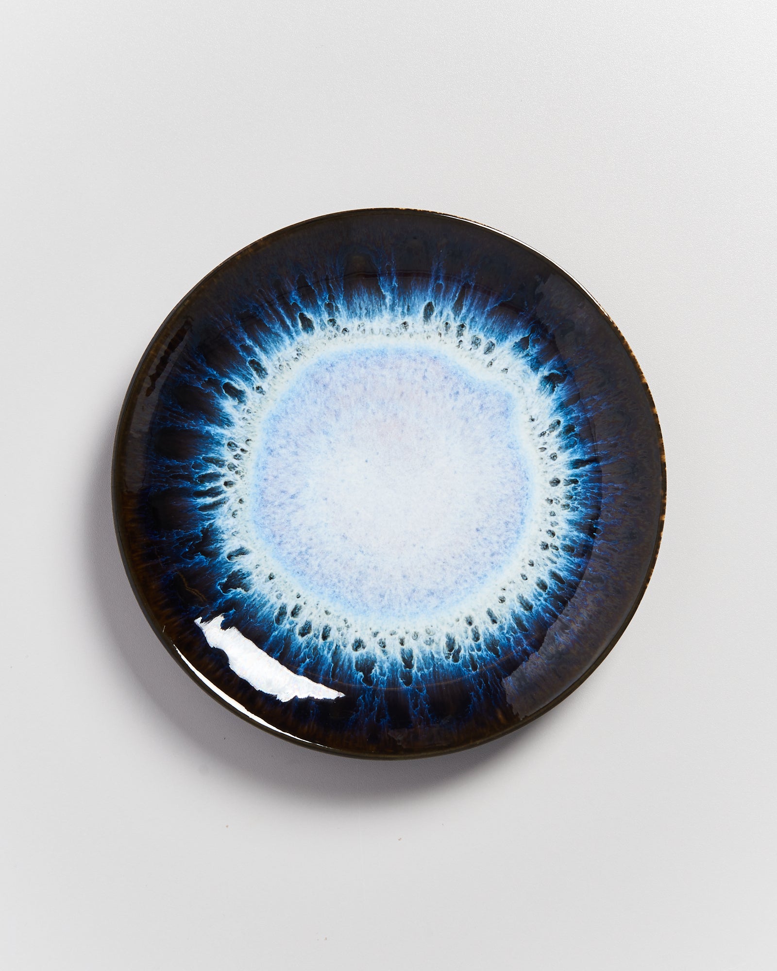 Keramikteller mit abstraktem, blauem Muster in der Mitte auf hellem Hintergrund.