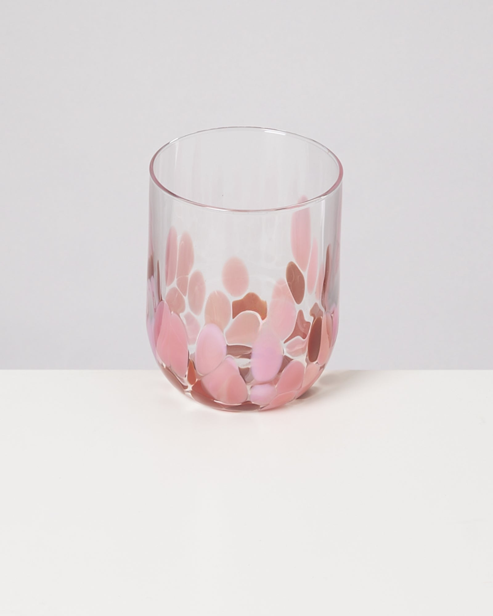 Ein Glas mit rosa und roten Tupfen steht auf einer weißen Oberfläche.