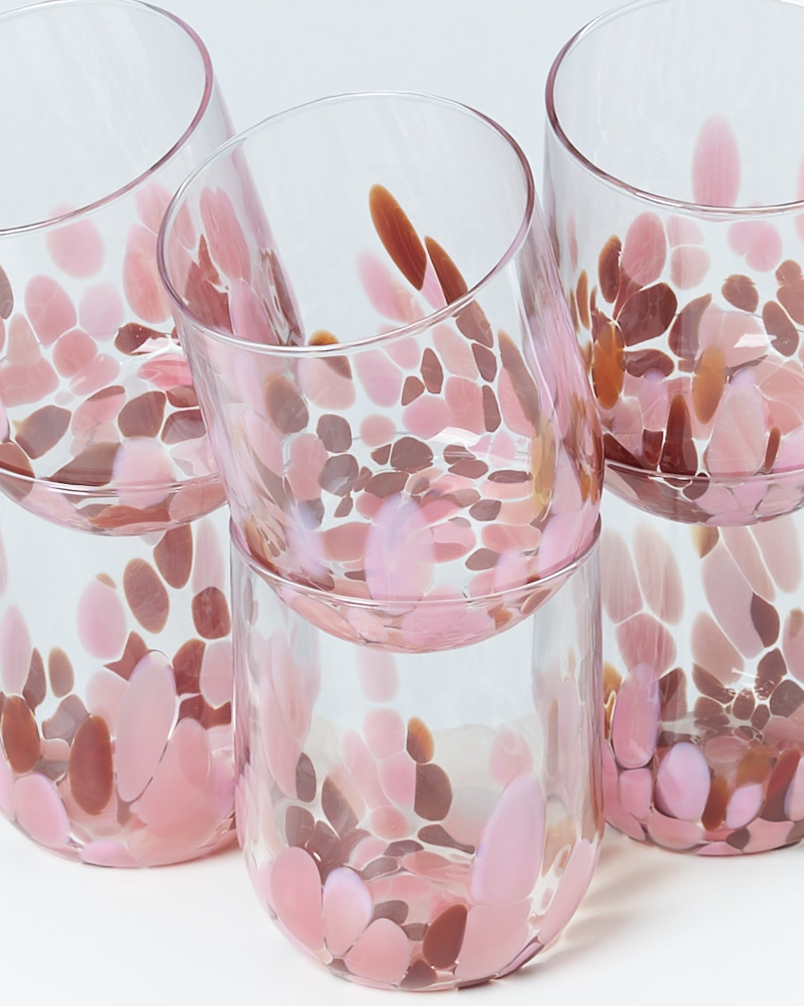 Vier Gläser mit rosa und braunen Punkten in einem organischen Muster gestapelt auf weißem Hintergrund.