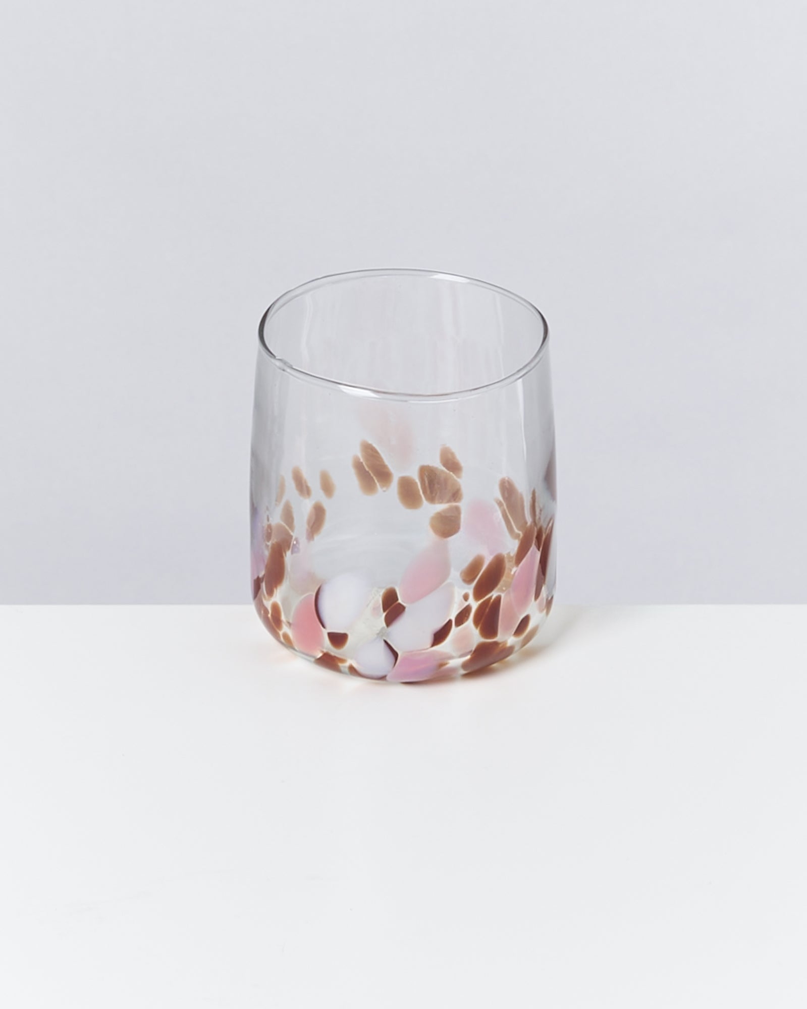 Ein durchsichtiges Glas mit bunten Tupfen in Braun-, Rosa- und Weißtönen steht auf einem weißen Tisch.