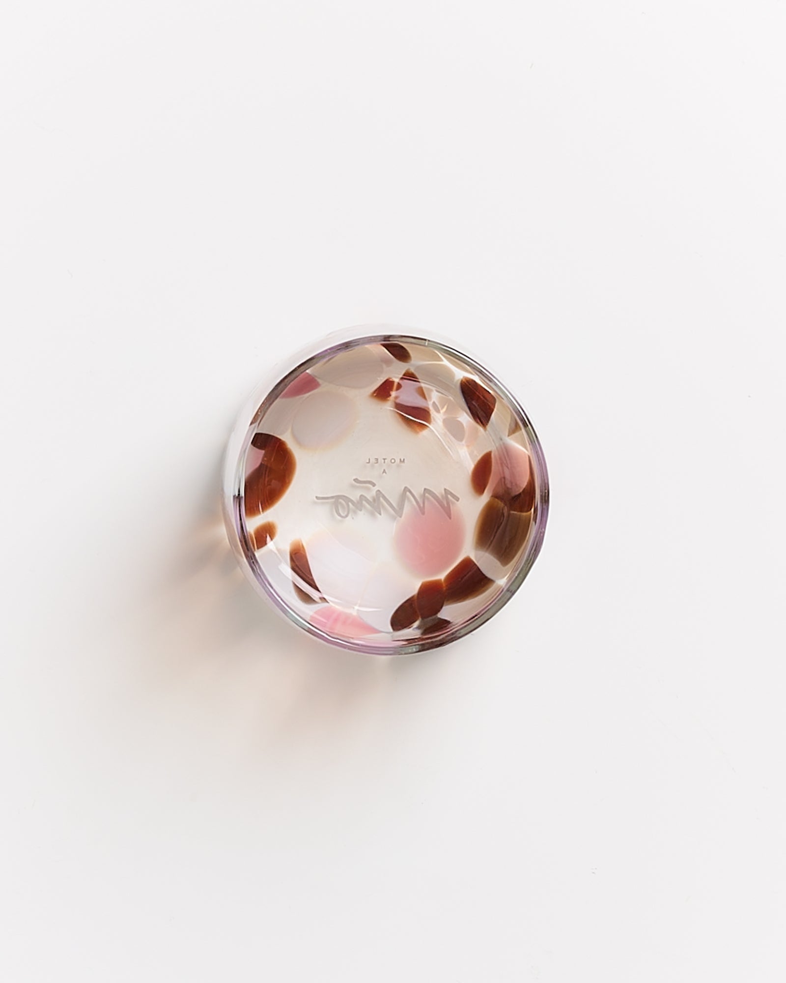 Runder durchsichtiger Glasgegenstand mit rosa und braunen Flecken auf weißem Hintergrund.