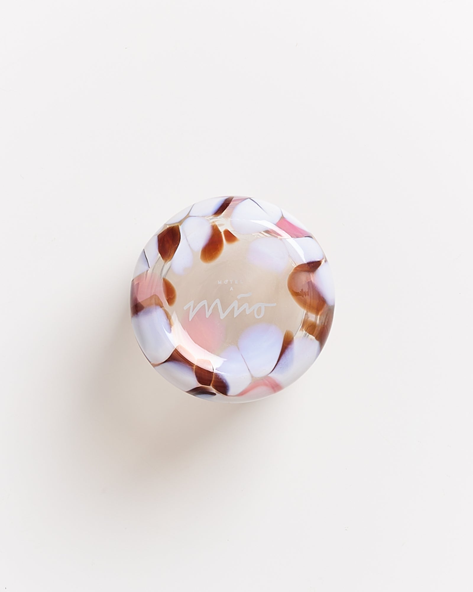 Runder, bunter Glasgegenstand mit marmoriertem Muster in Braun-, Weiß- und Rosatönen auf weißem Hintergrund.