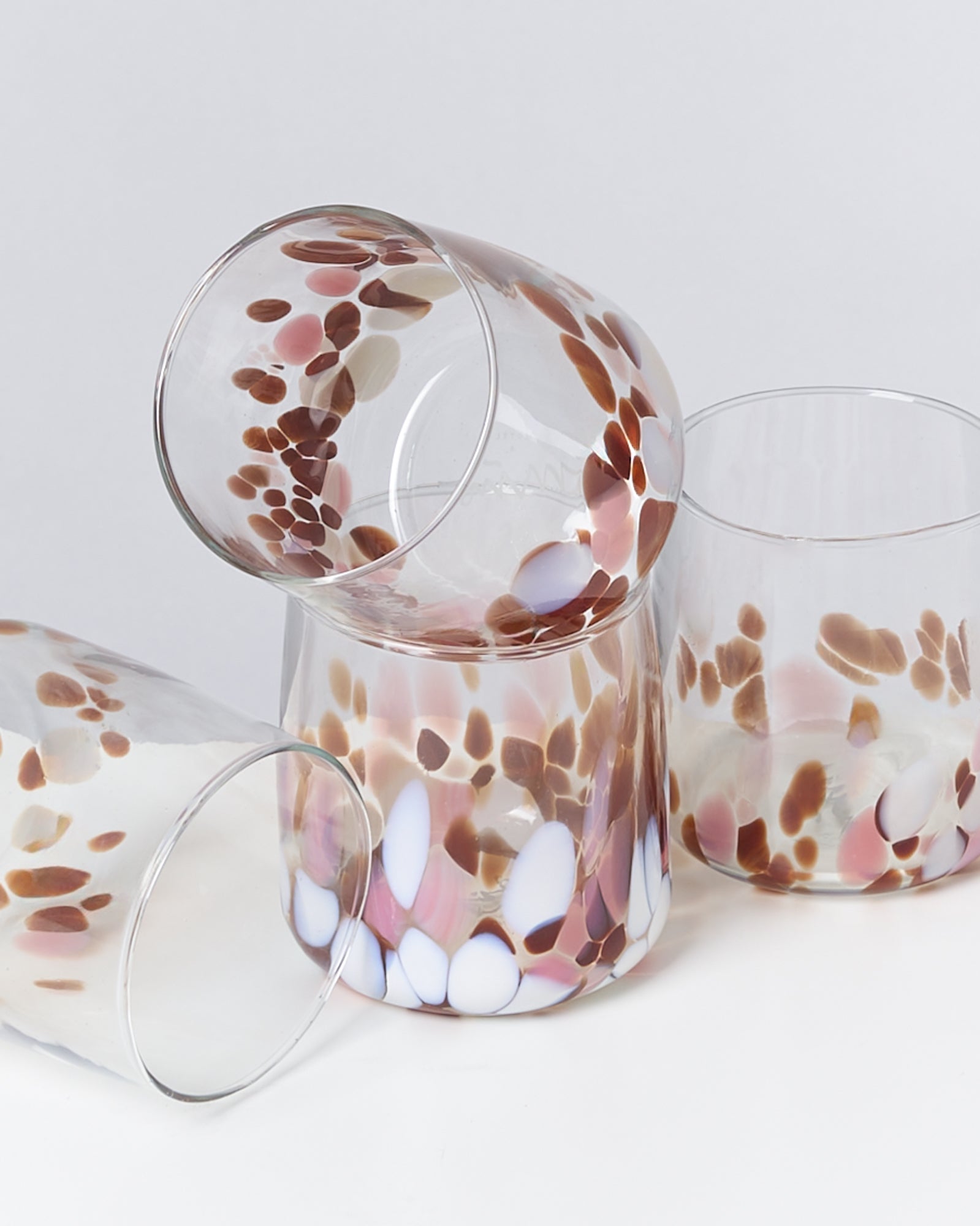 Vier bunte Glasbecher mit braunen und weißen Mustern auf weißem Hintergrund.