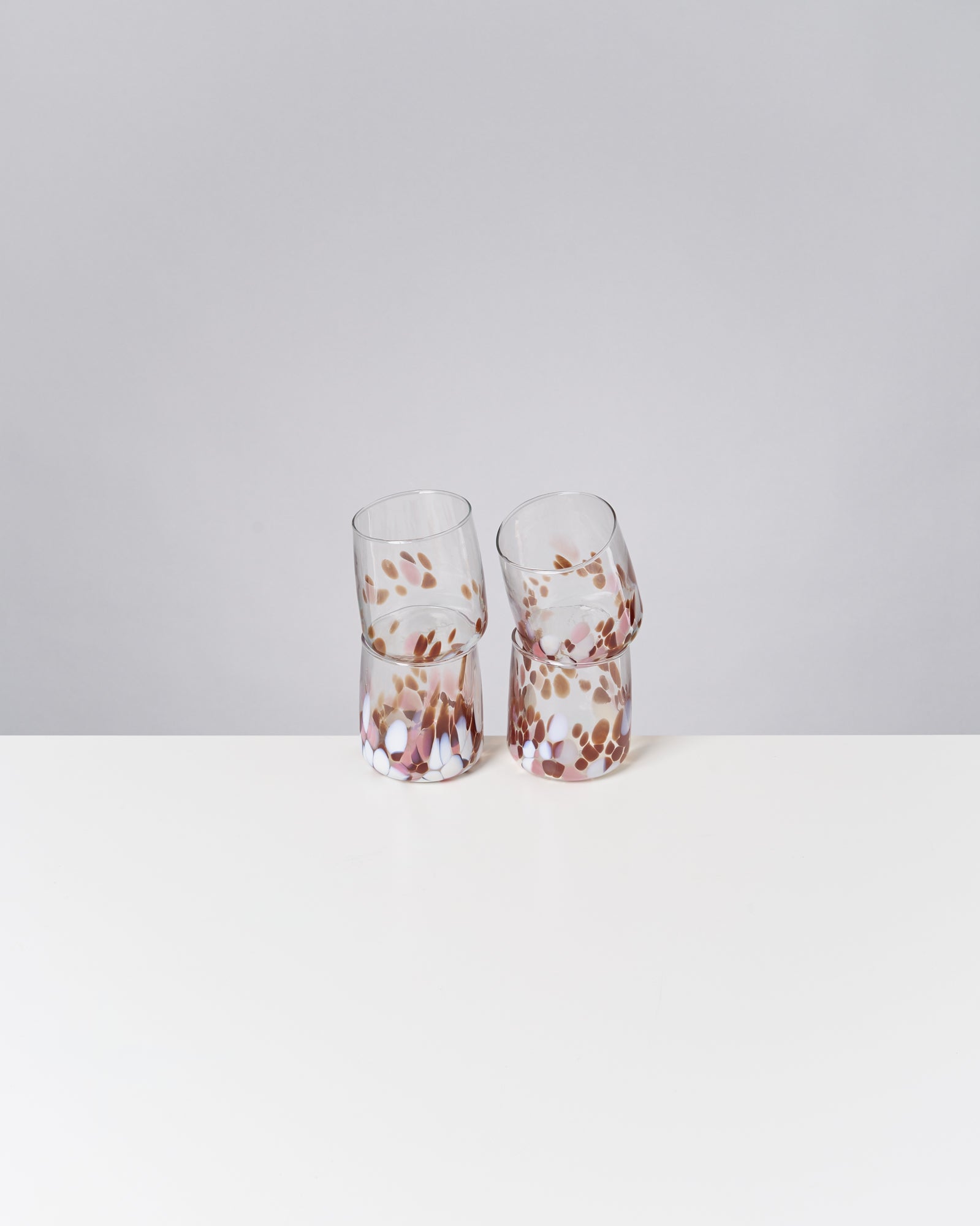 Vier bunte Gläser mit gepunktetem Muster stehen auf einem weißen Tisch vor grauem Hintergrund.