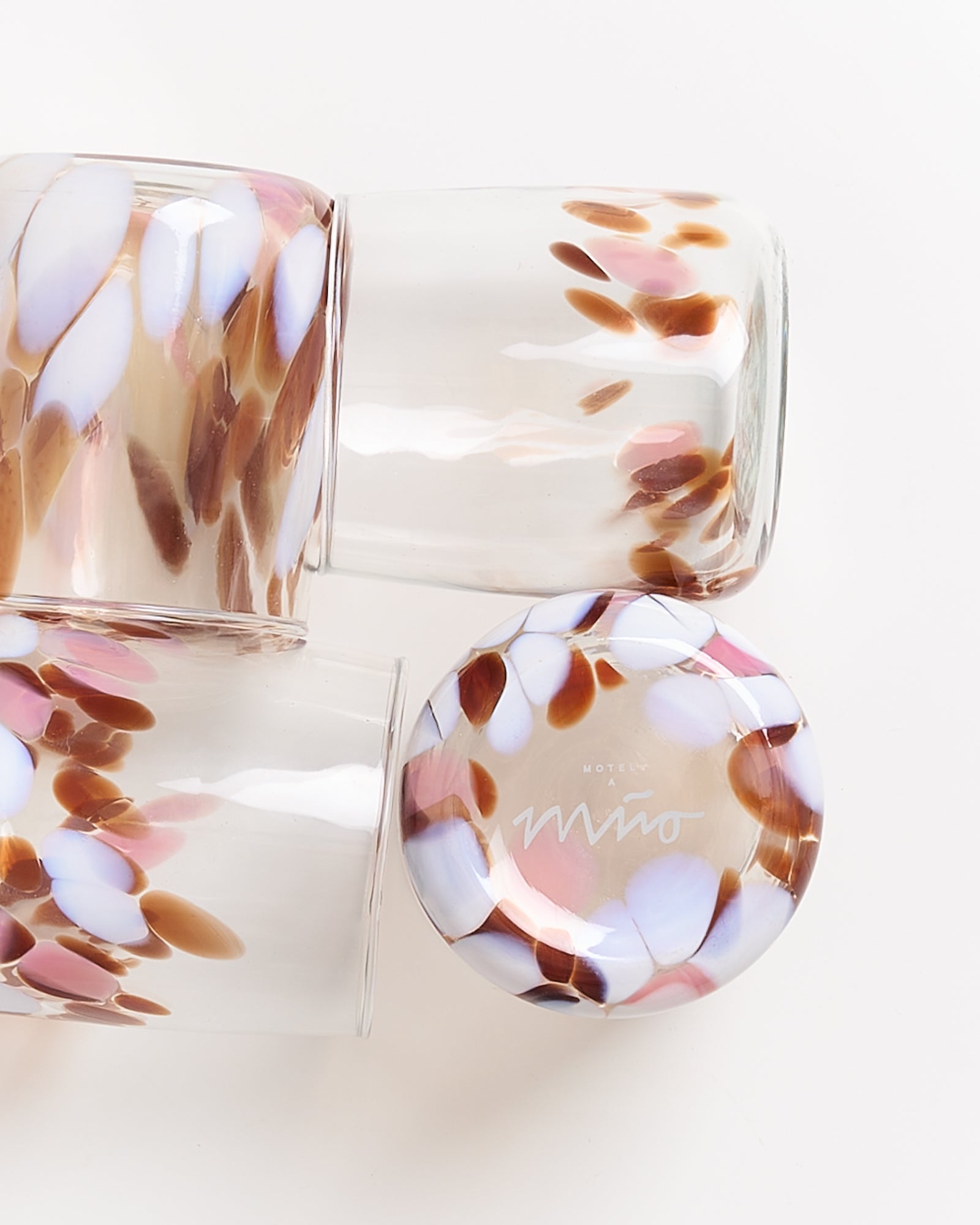 Drei gläserne Becher mit braun-weißem Tupfenmuster liegen gestapelt auf einer hellen Oberfläche.