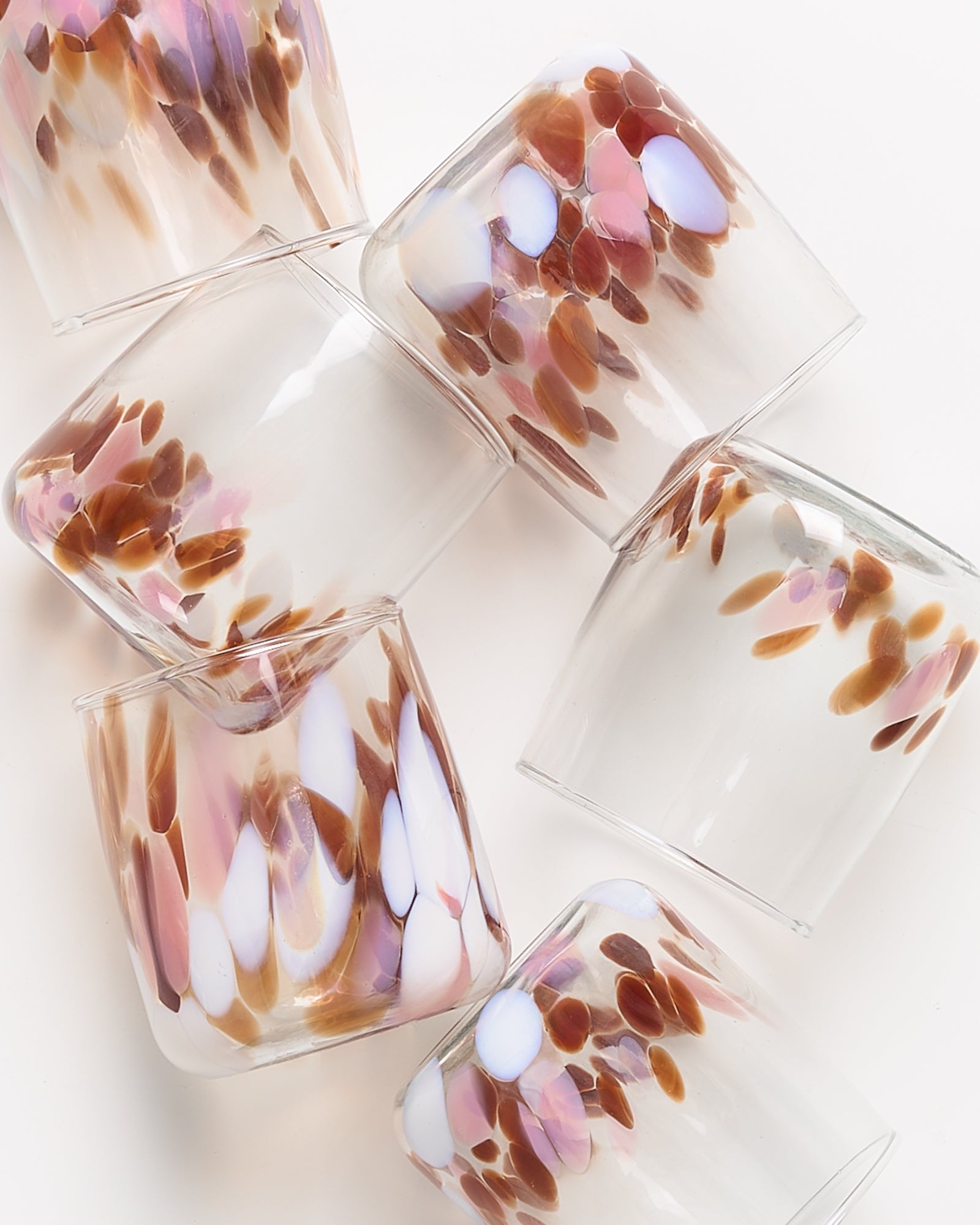 Mehrere durchsichtige Gläser mit bunten, gefleckten Mustern in Braun, Weiß und Rosa, unregelmäßig gestapelt.