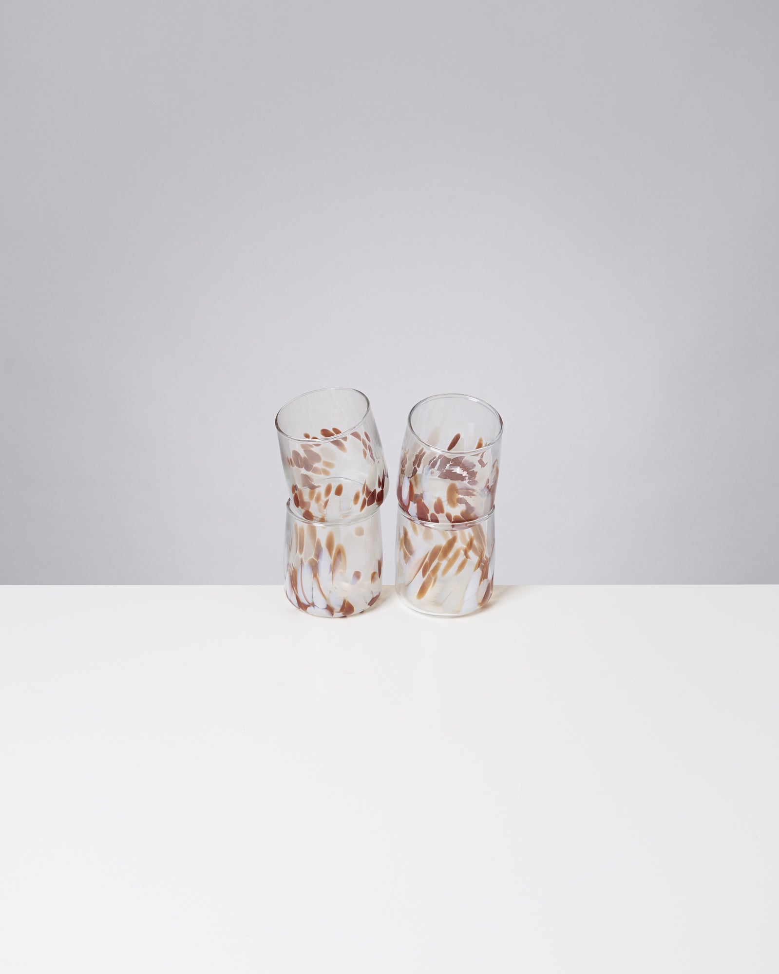 Zwei geschwungene Gläser mit braunem und weißem Muster stehen auf einem weißen Tisch vor grauem Hintergrund.