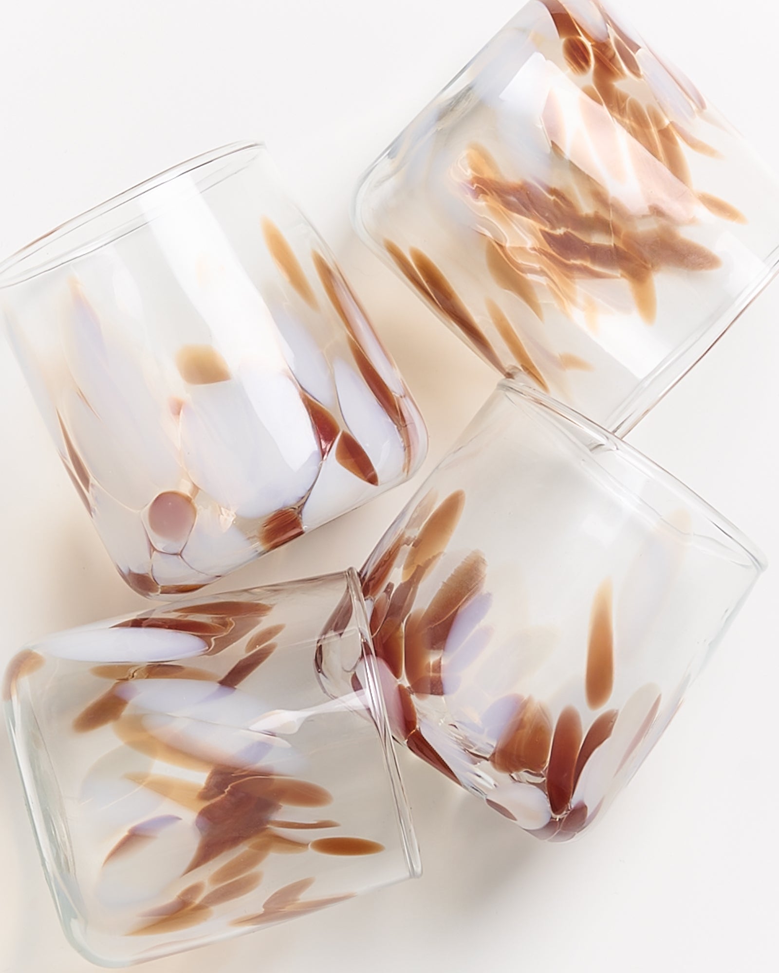 Vier Glasbecher mit braunen und weißen Mustern liegen nebeneinander auf einer weißen Oberfläche.