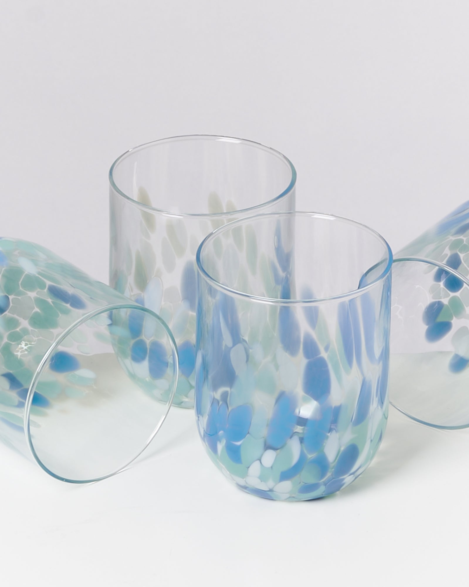 Vier bunte Gläser mit blauen und grünen Tupfen auf weißem Hintergrund.