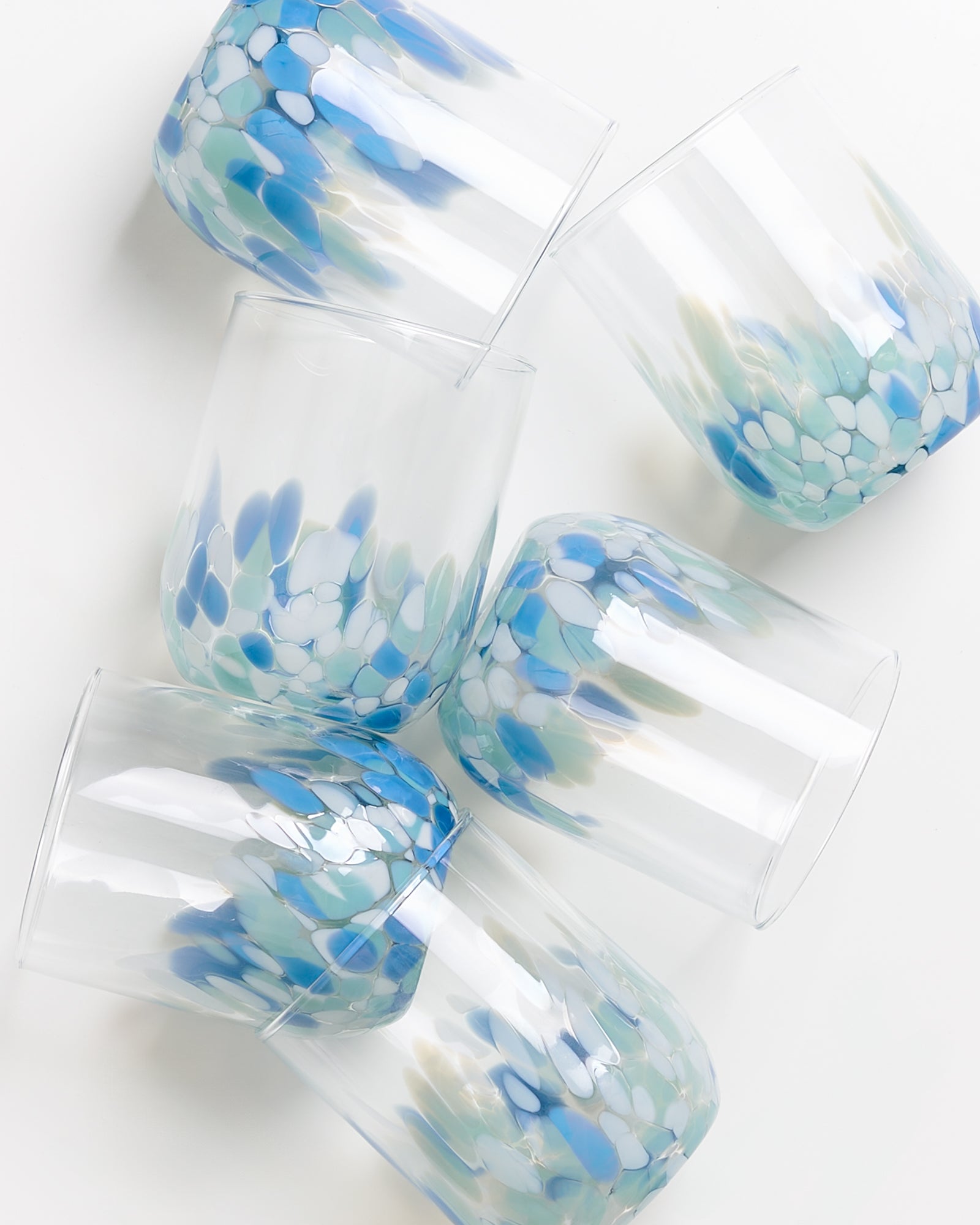 Sechs bunte Gläser, teilweise mit blauen und grünen Flecken, liegen auf einer weißen Fläche.