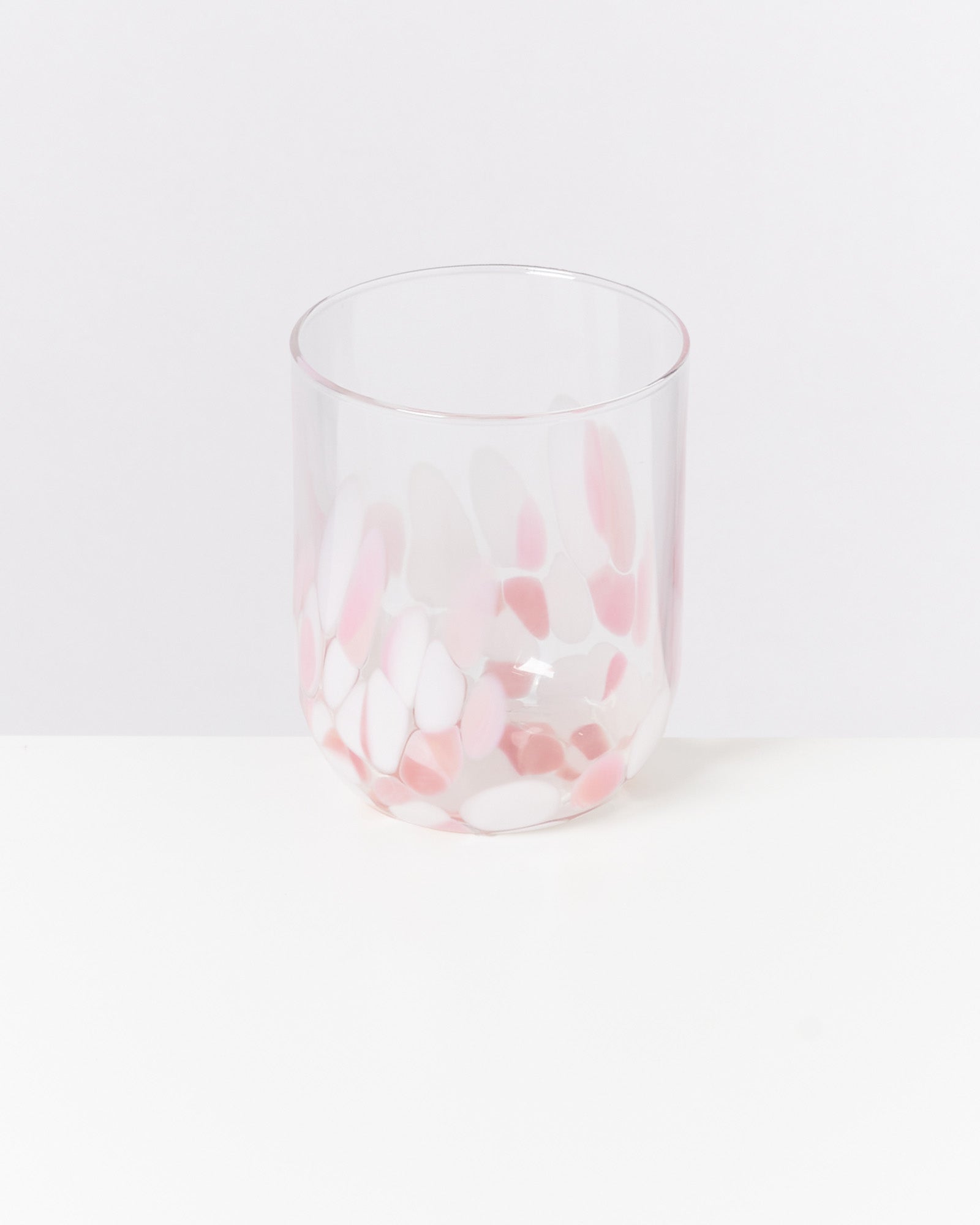 Ein transparentes Glas mit rosa- und weißfarbenen Mustern auf einer weißen Oberfläche.