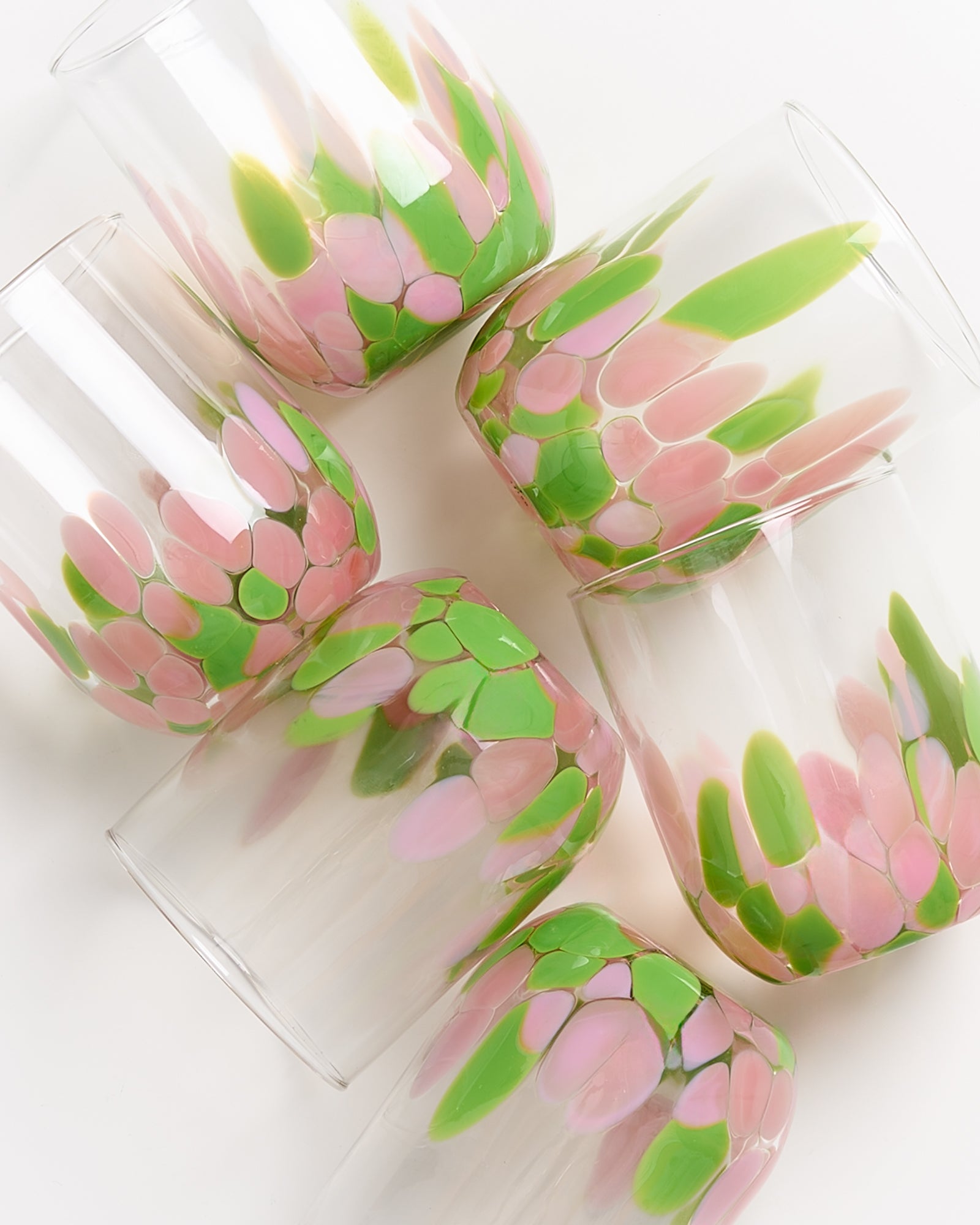Sechs Gläser mit rosa und grünen Mustern auf einer weißen Oberfläche angeordnet.
