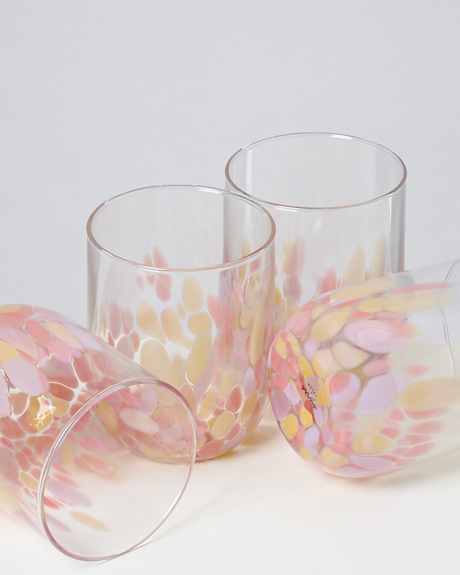 Vier bunte Gläser mit rosa und gelben Flecken, teilweise liegend und stehend auf weißem Hintergrund.