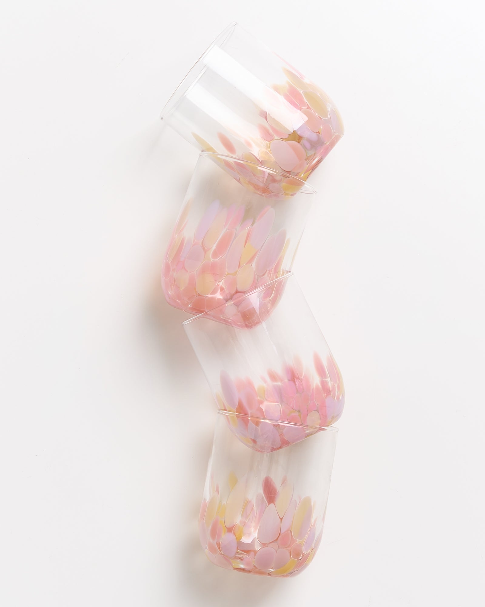Vier gläserne Becher mit rosa und gelben Flecken, die übereinander gestapelt sind, stehen auf einer weißen Fläche.