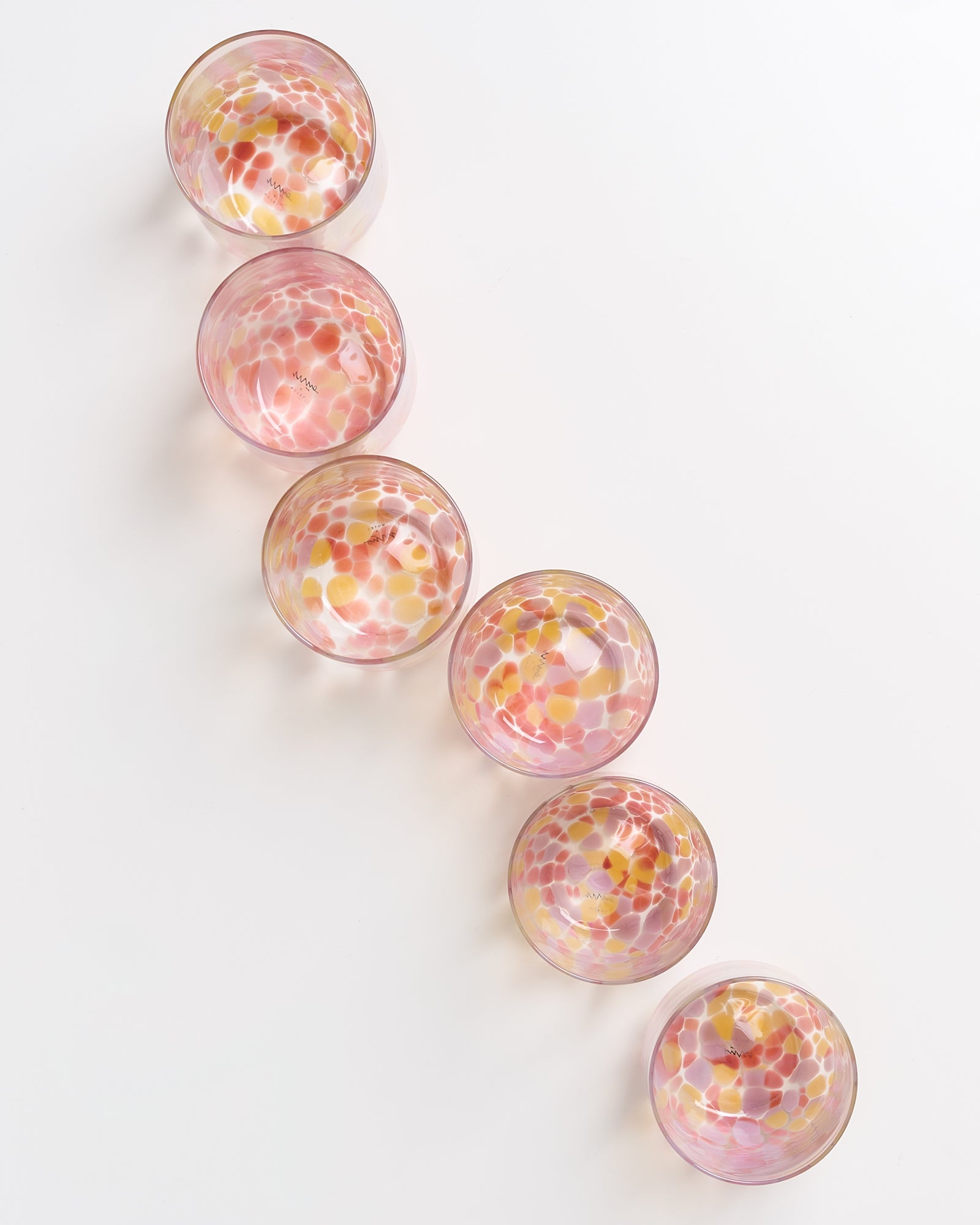 Sechs bunte Glasschalen mit Mosaikmuster in Rosa, Gelb und Weiß, diagonal angeordnet auf weißem Hintergrund.