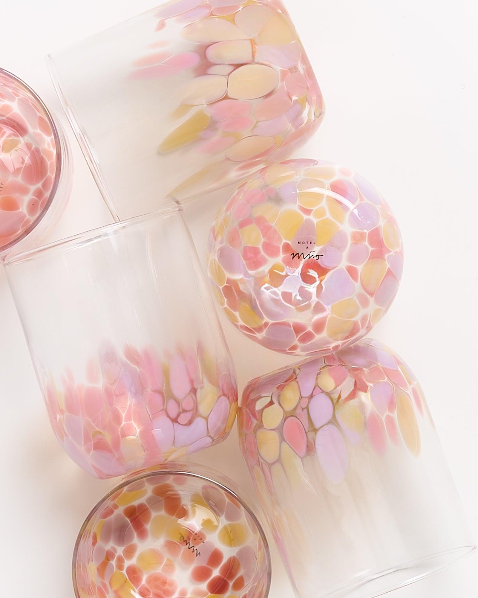 Sechs gläserne Becher mit buntem, marmoriertem Muster in Rosa, Gelb und Weiß auf weißem Hintergrund.
