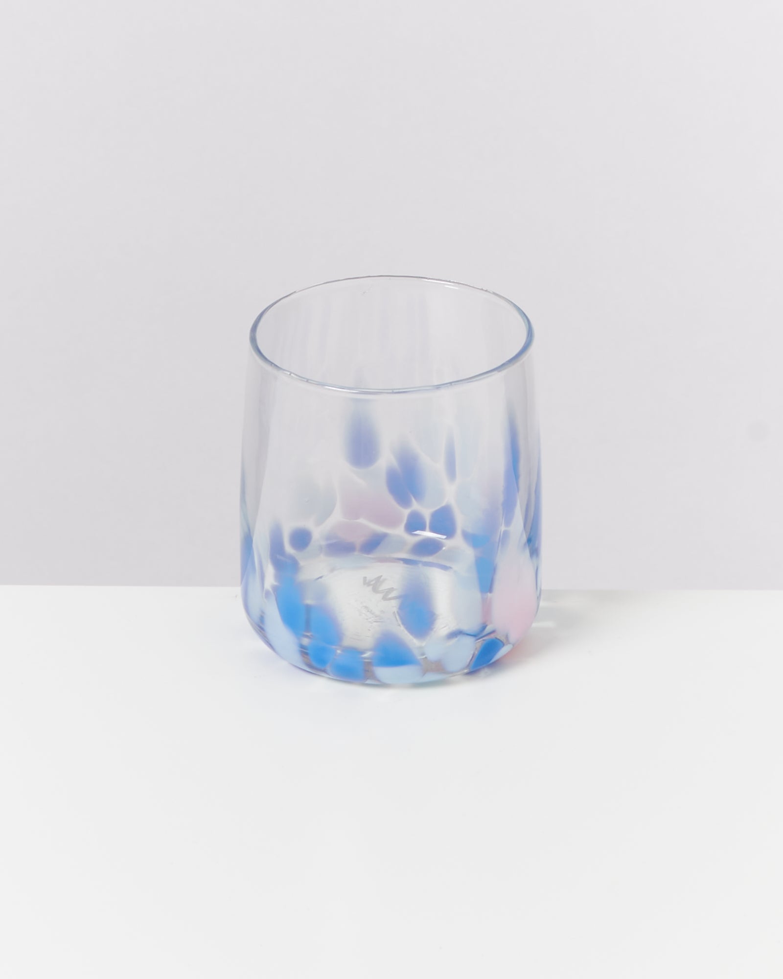 Ein Glas mit blauen und violetten Flecken steht auf einem weißen Tisch vor einem weißen Hintergrund.