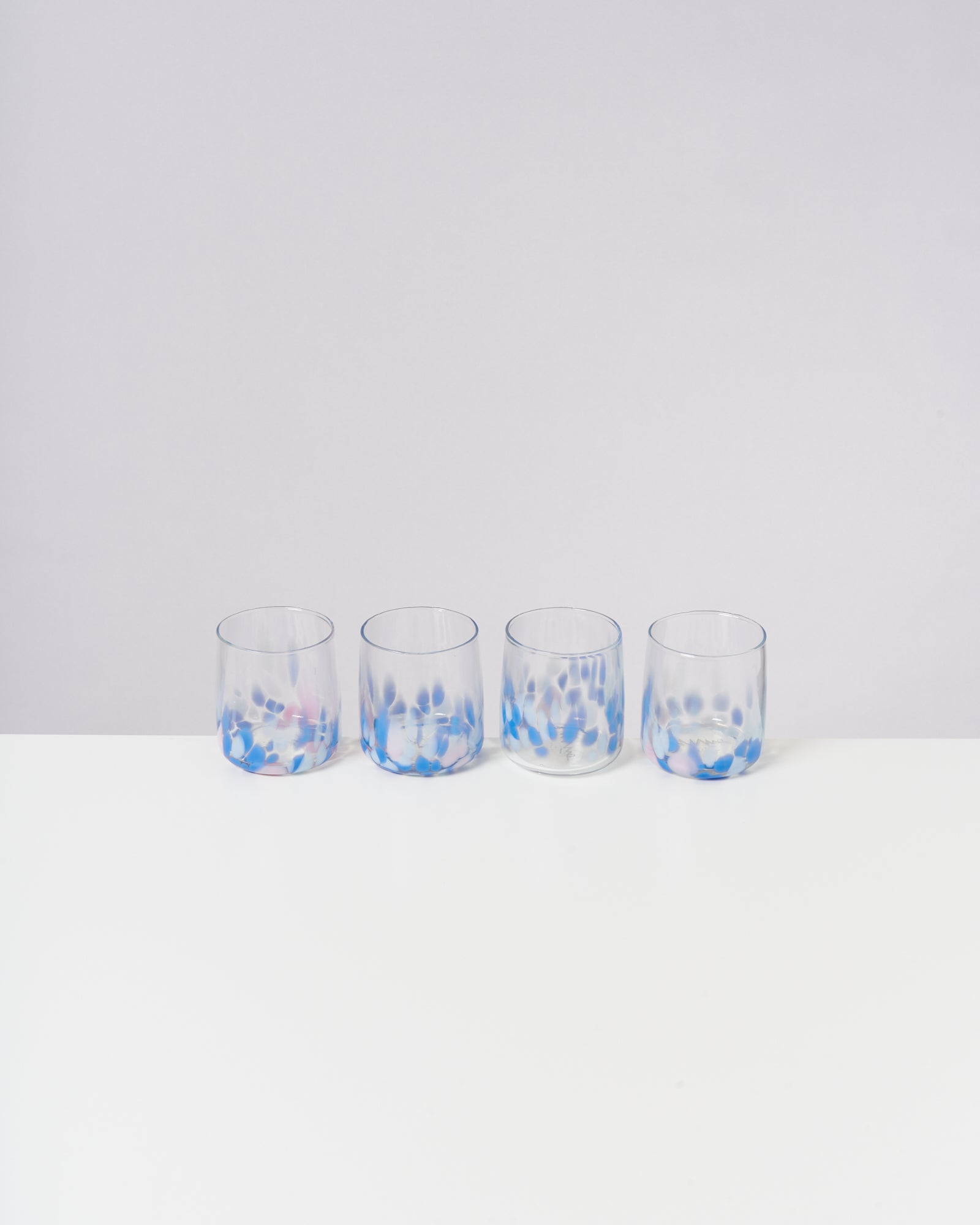 Vier Gläser mit blauem Tupfenmuster stehen in einer Reihe auf einem weißen Tisch.
