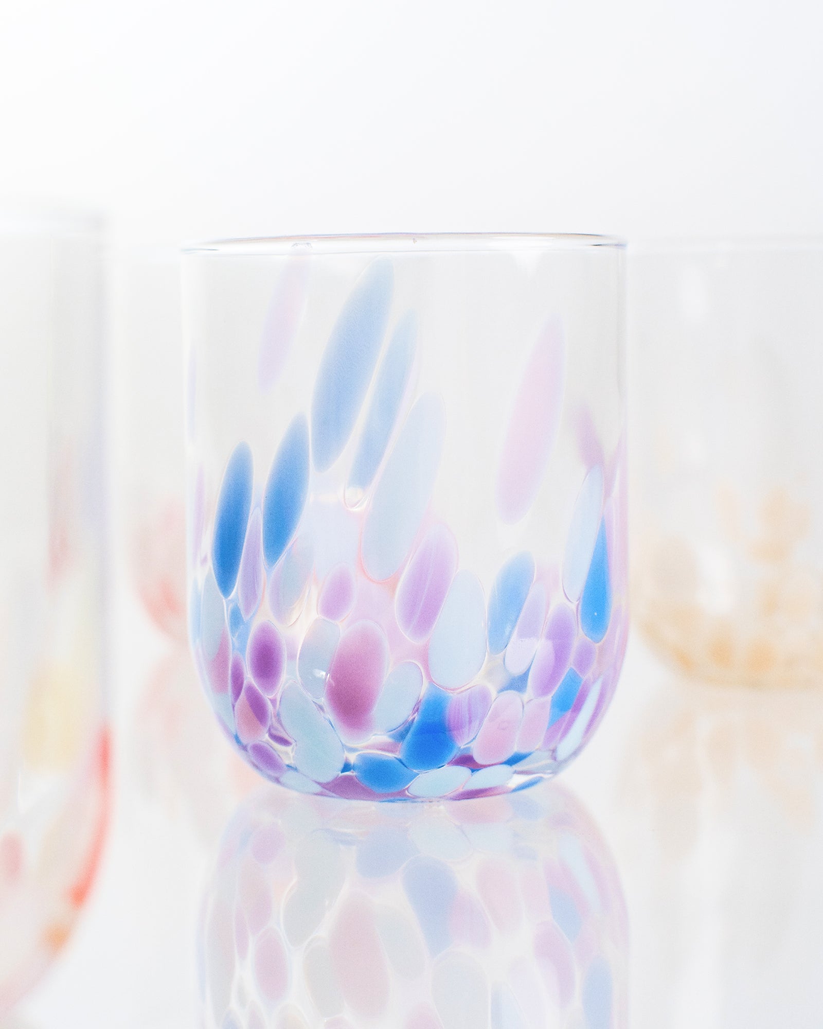 Ein Glas mit bunten, abstrakten Mustern in Blau, Rosa und Lila vor einem weißen Hintergrund.
