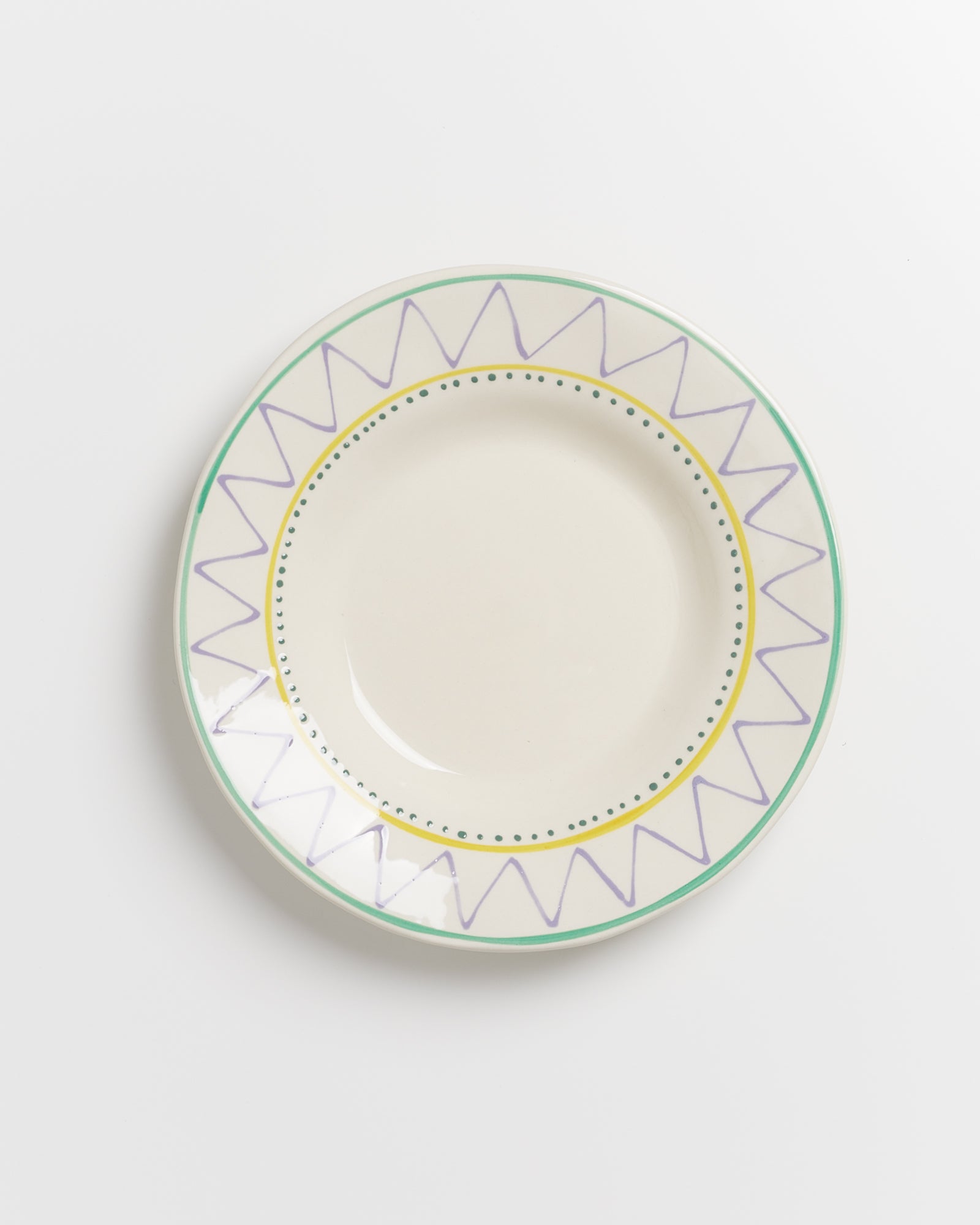 Teller mit grünem Rand und gelbem, gezacktem Muster, verziert mit lila Linien auf hellem Hintergrund.