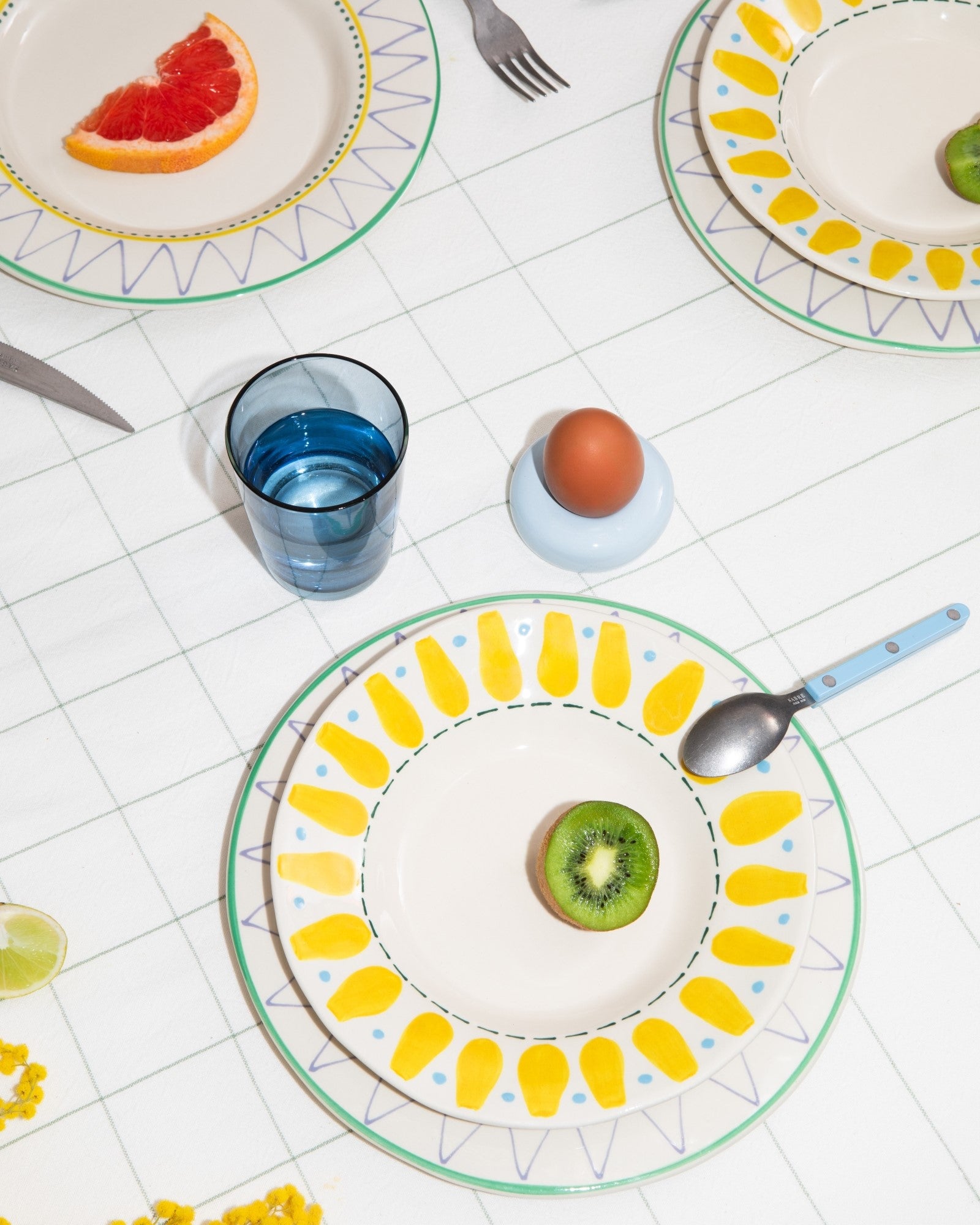 Ein Tisch mit dekorativen Tellern, einem halben Kiwi, einem halben Grapefruit, einem Ei, einem Glas Wasser und Besteck.