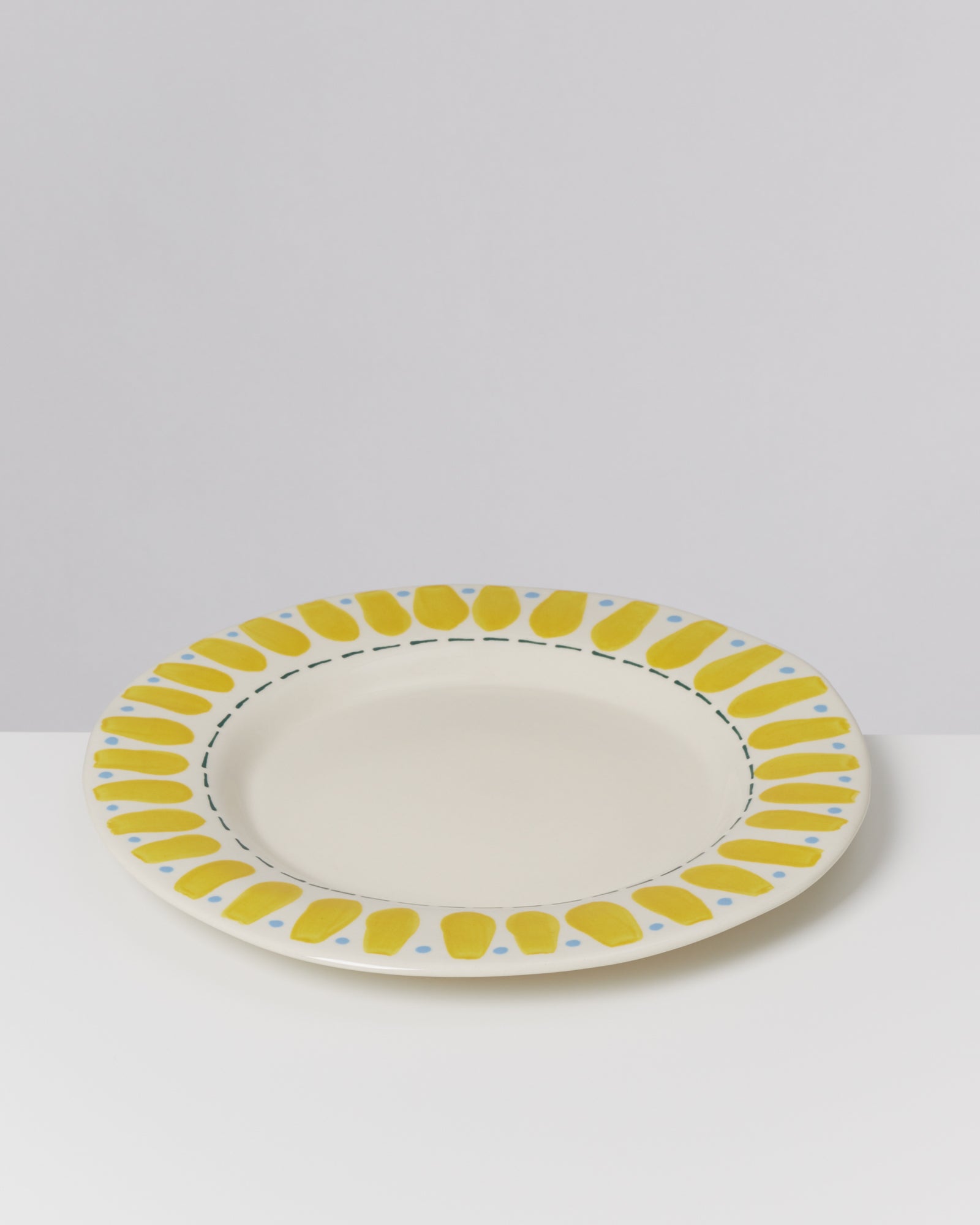 Ein Teller mit gelbem und blauem Muster auf einer weißen Oberfläche vor grauem Hintergrund.