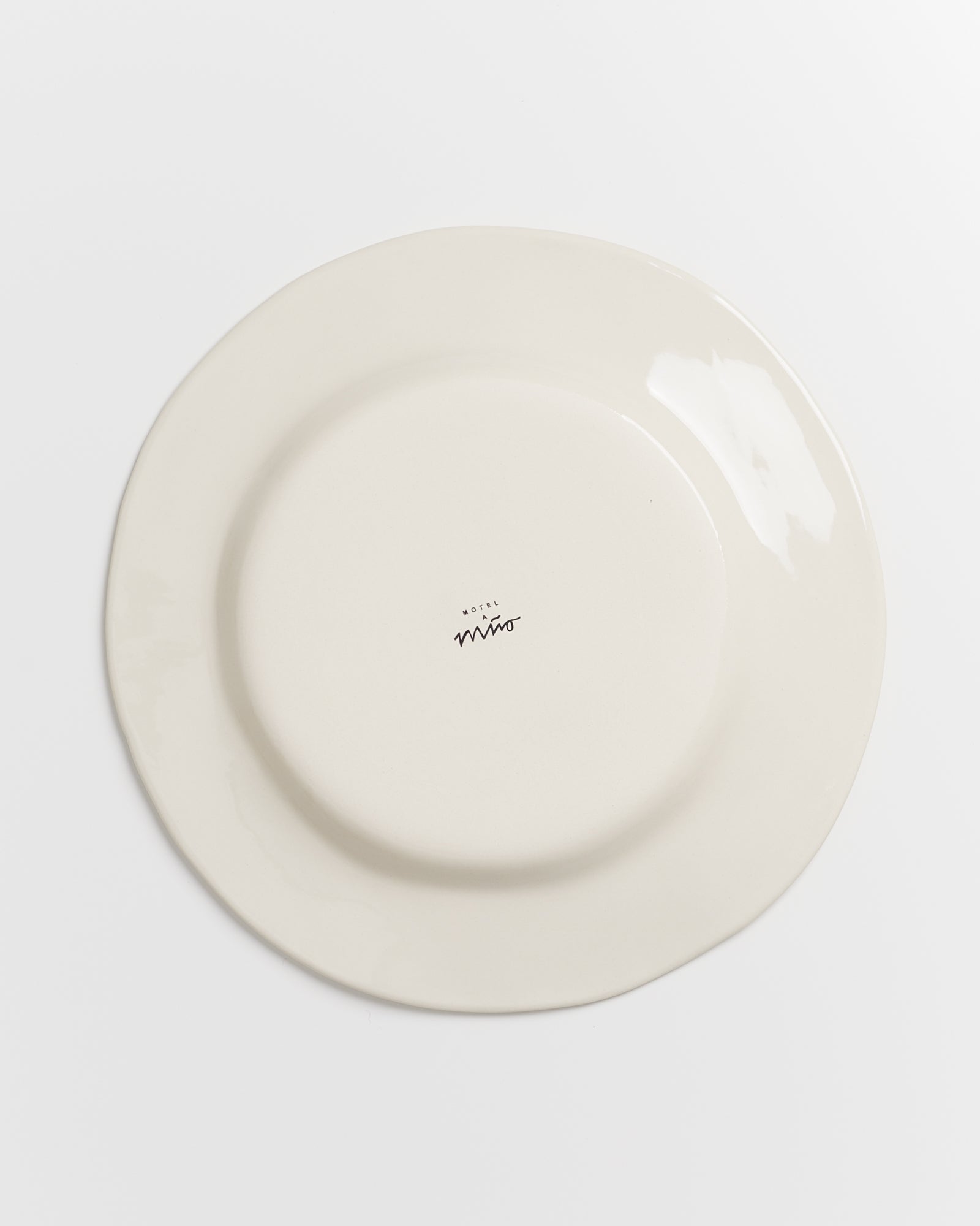 Rückseite eines weißen Tellers mit schwarzem Aufdruck "Hotel" und unleserlichem Schriftzug, auf weißem Hintergrund.