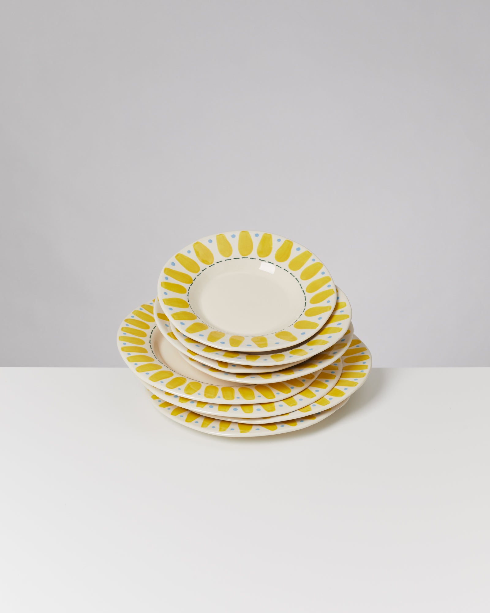 Gestapelte Teller mit gelbem und blauem Muster auf einem weißen Tisch vor grauem Hintergrund.