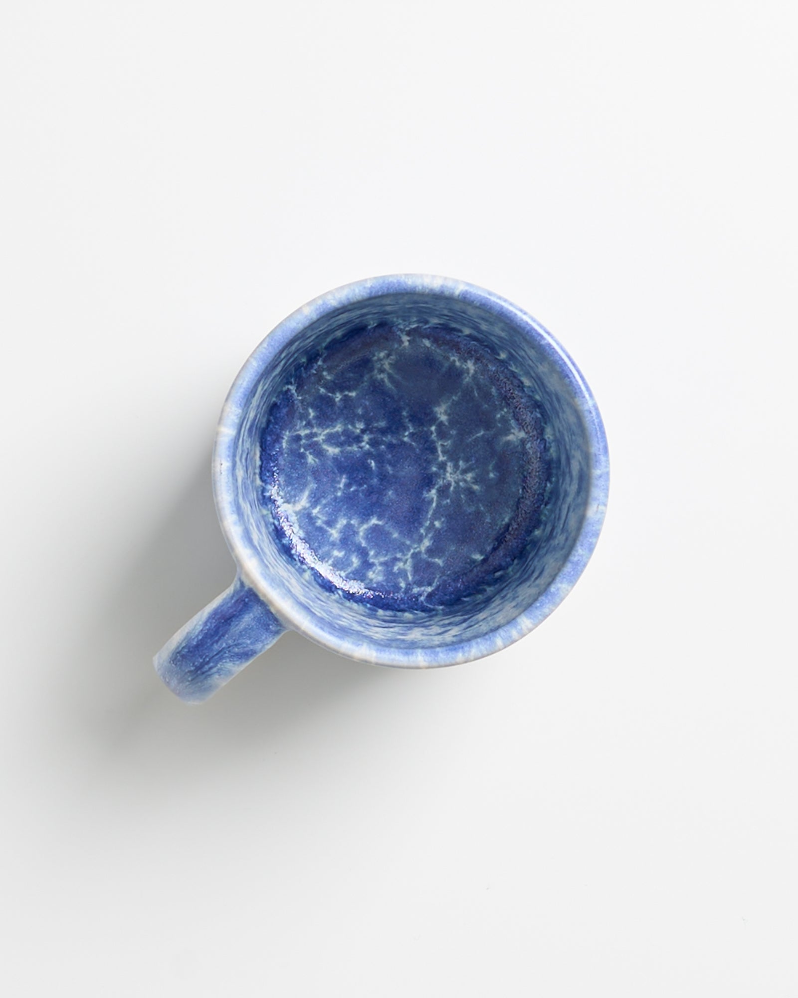 Blaue Tasse mit marmoriertem Muster von oben auf weißem Hintergrund.