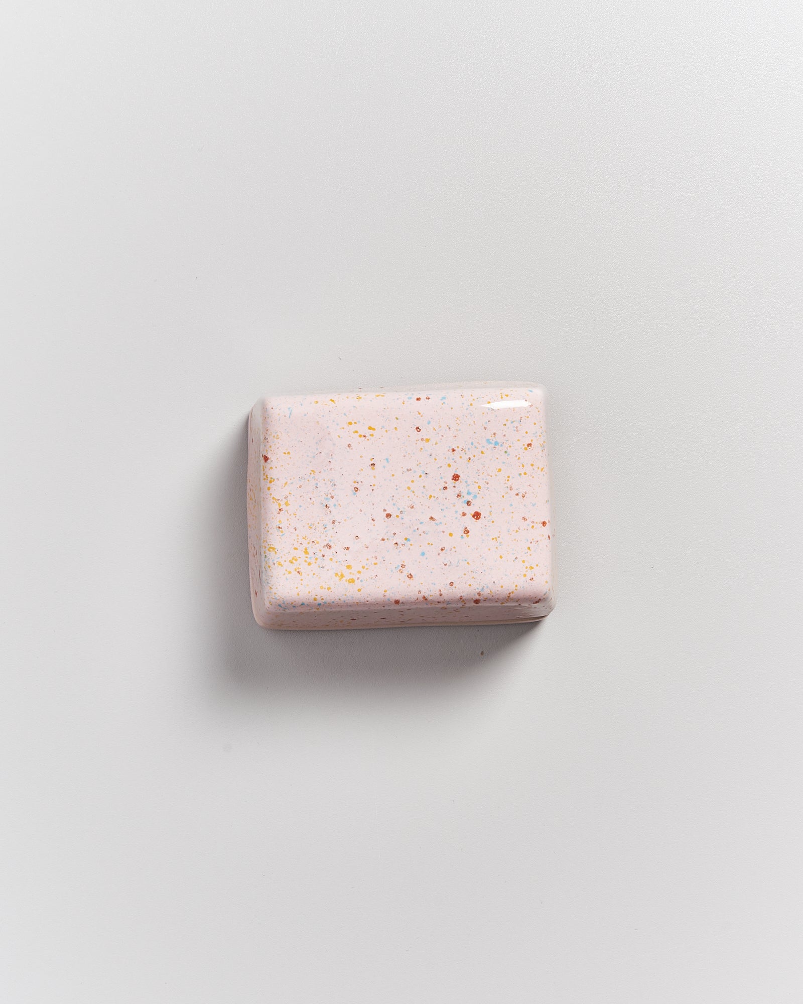 Rechteckige rosa Specksteinseife mit bunten Sprenkeln auf einer weißen Oberfläche.