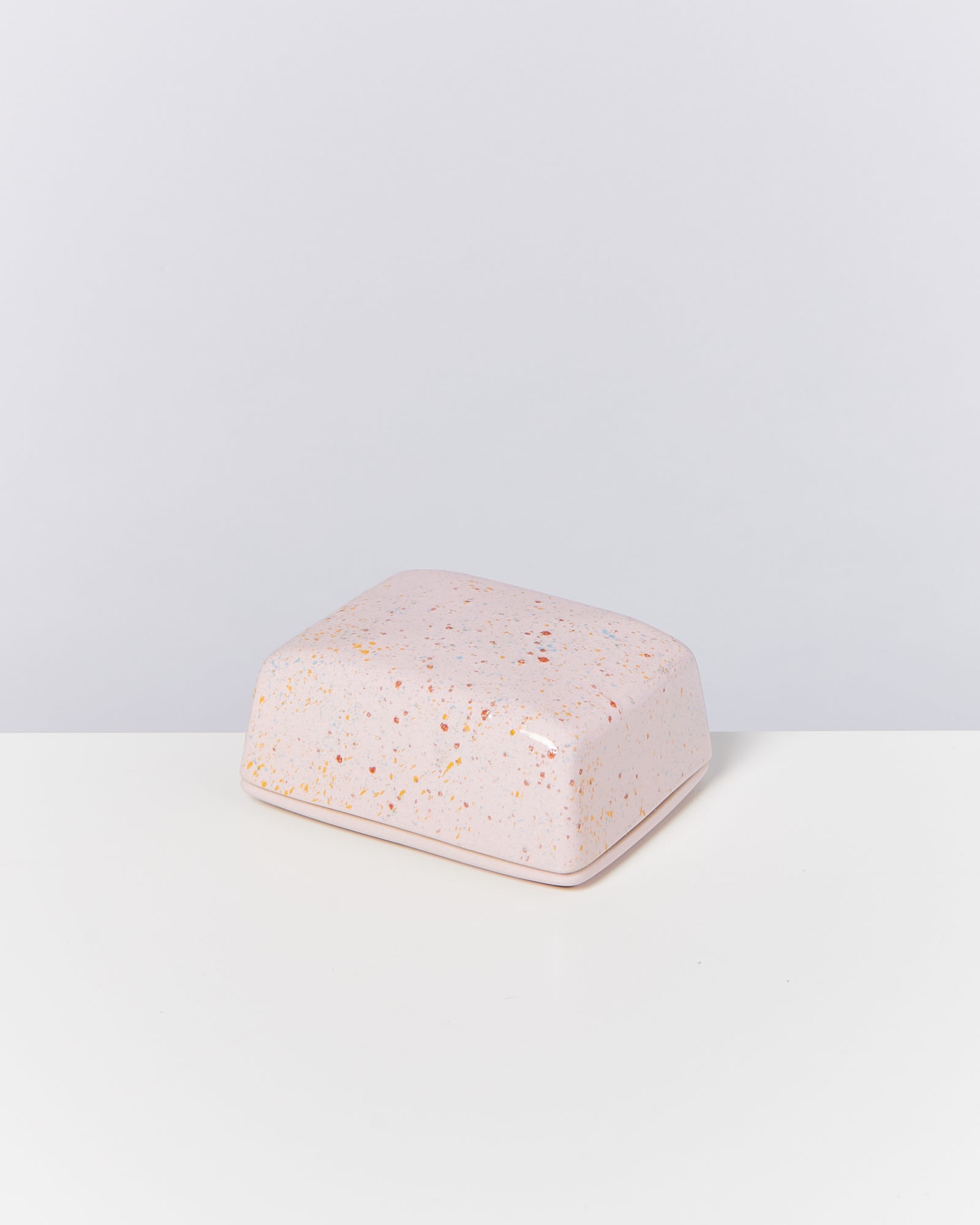 Rosa, rechteckige Keramikdose mit bunten Sprenkeln steht auf weißem Untergrund.