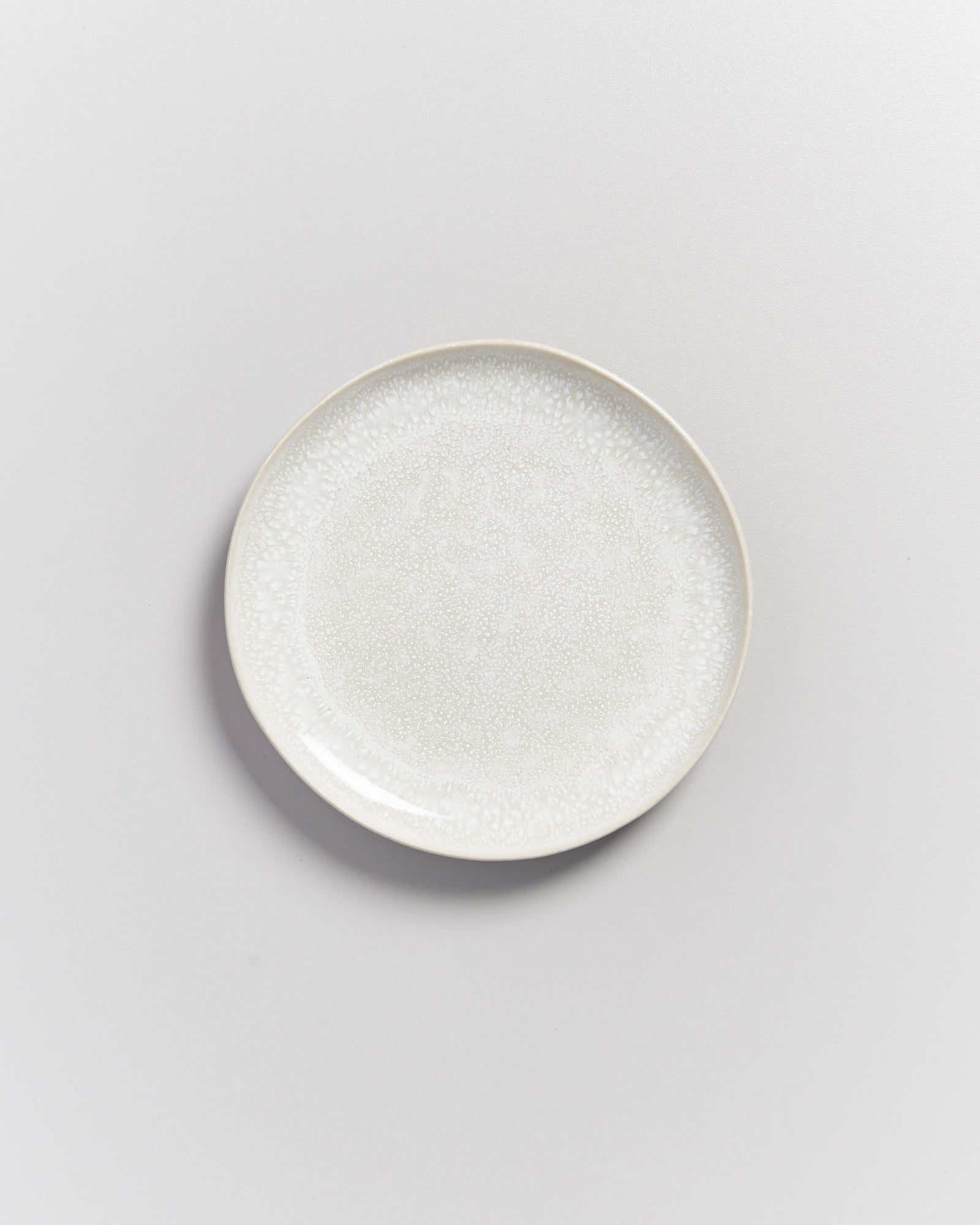 Weißer Keramikteller mit dezenter Musterung auf einer weißen Oberfläche.