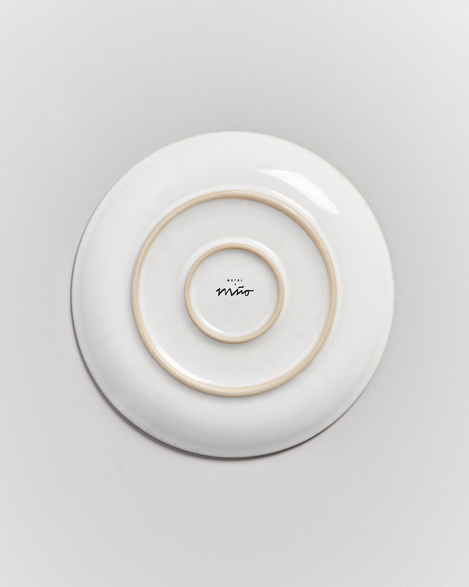 Eine weiße Untertasse mit konzentrischen Kreisen und einer kleinen Aufschrift in der Mitte auf einer grauen Oberfläche.