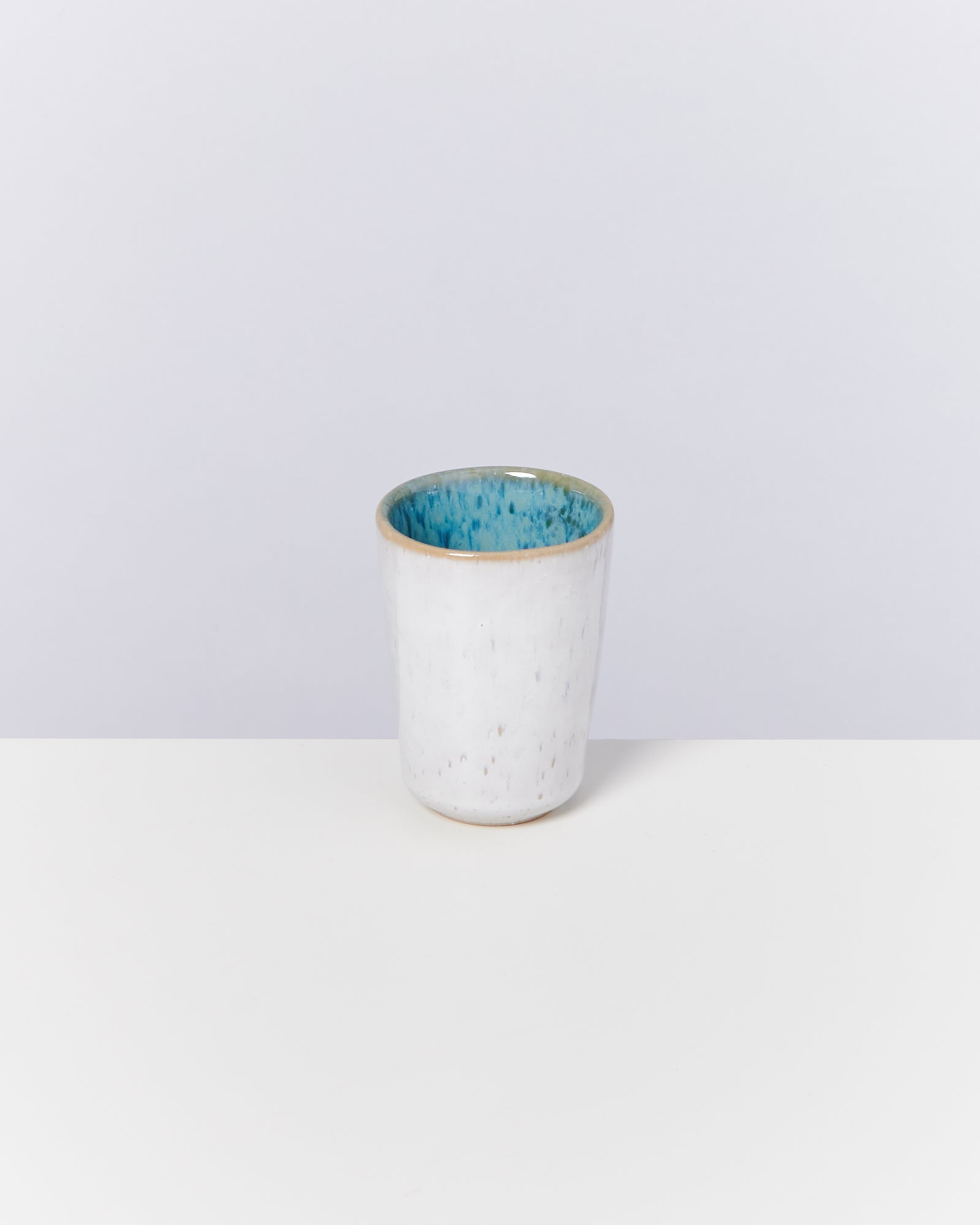 Weiße Keramiktasse mit blauem Innenbereich auf weißem Hintergrund.