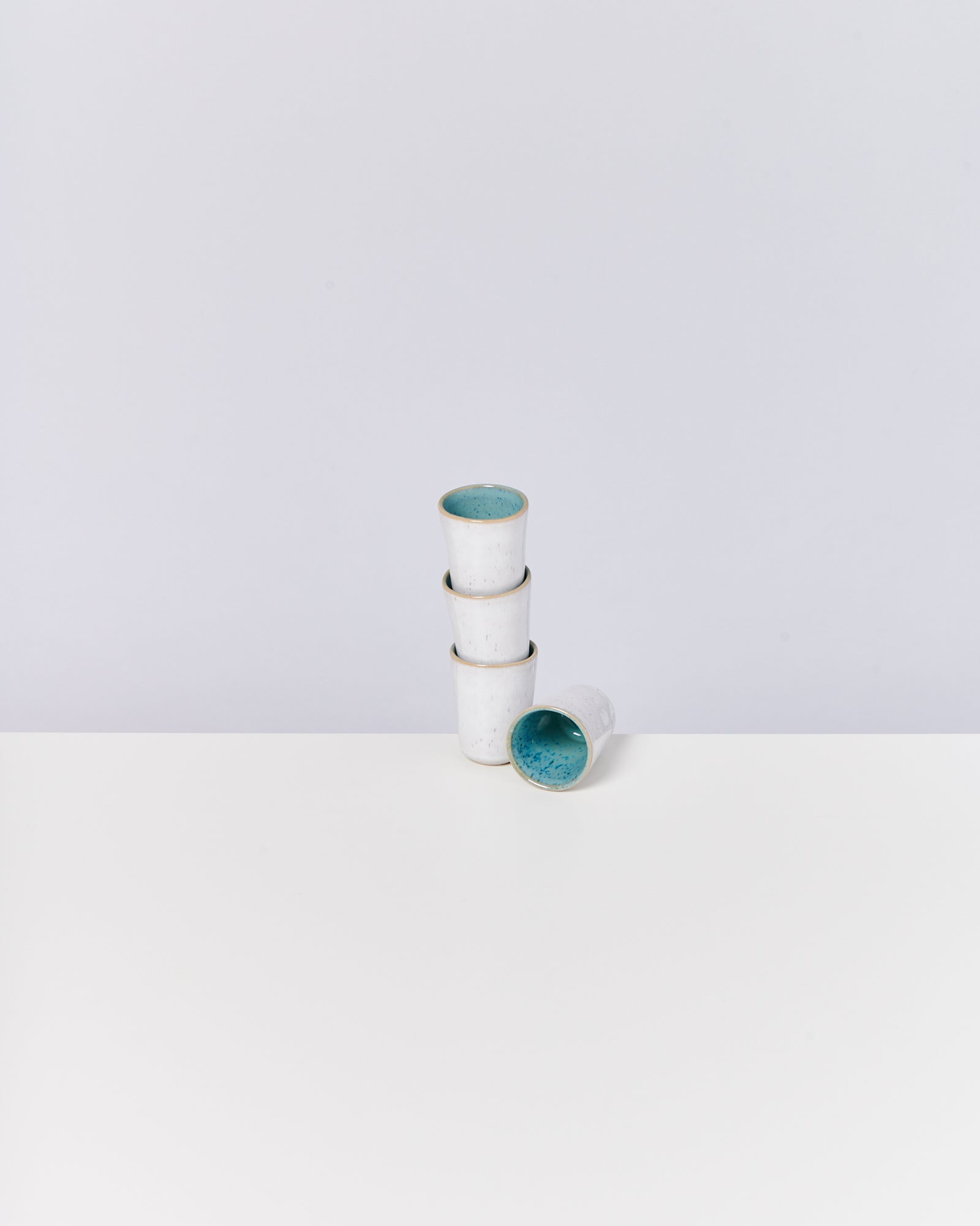 Drei gestapelte weiße Becher mit blauer Innenseite, ein Becher liegt quer, auf einem weißen Hintergrund.