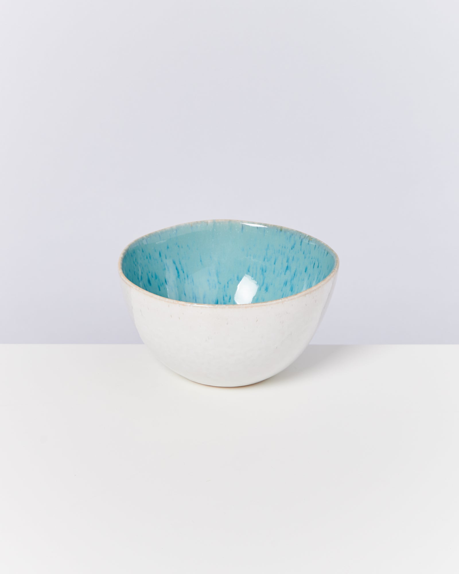 Eine Keramikschale mit weißem Äußeren und blauem Inneren steht auf einem weißen Tisch.