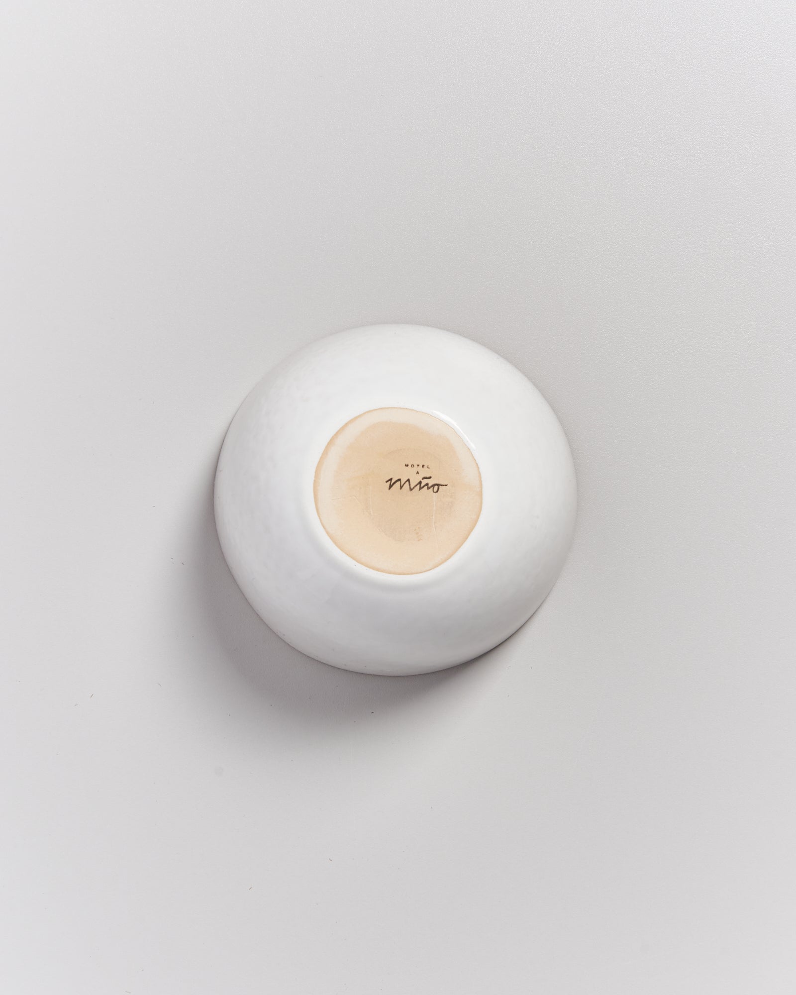 Umgedrehte weiße Schale auf einer hellen Oberfläche mit einem gestempelten Logo in der Mitte des Bodens.