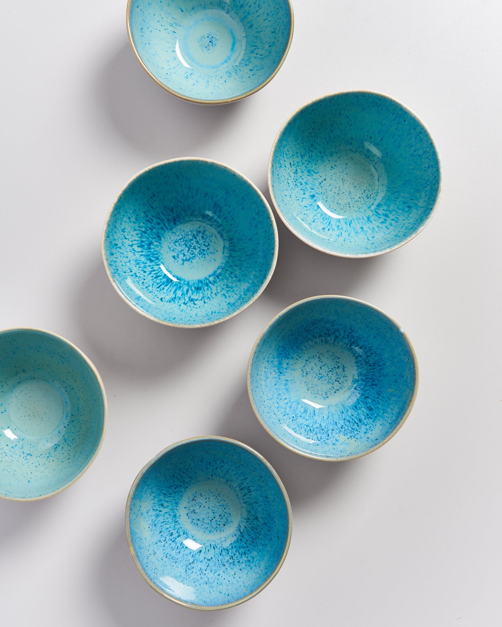 Sechs blaue, gepunktete Schalen auf einer weißen Oberfläche, unregelmäßig angeordnet.
