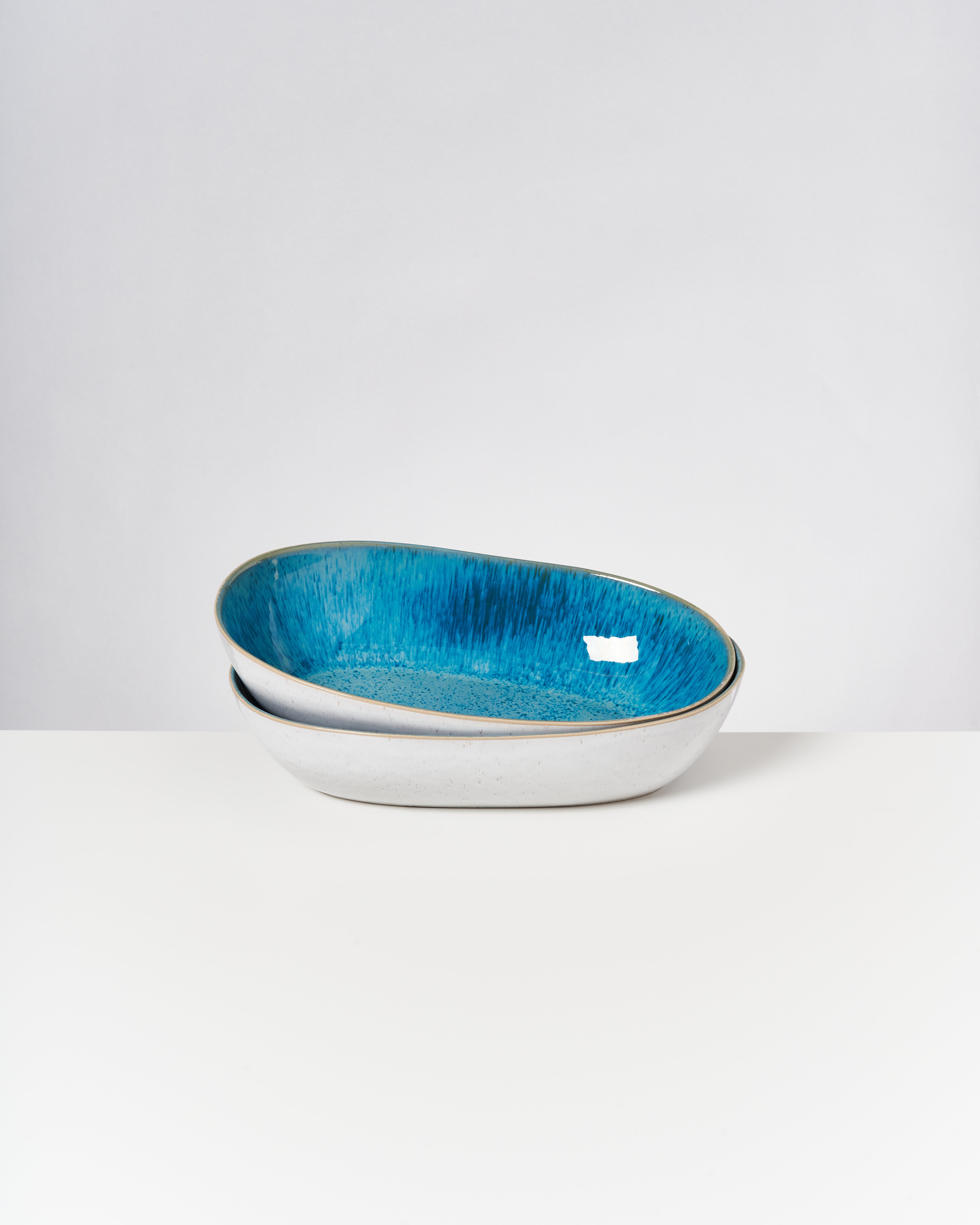 Zwei stapelbare, ovale Schalen mit blauem Innenraum stehen auf einem weißen Tisch.