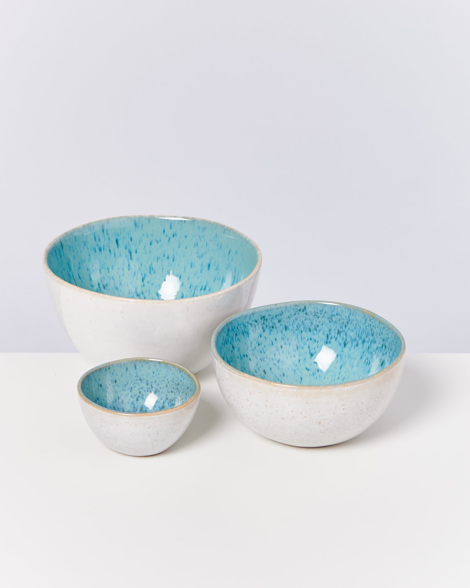 Drei Keramikschalen in verschiedenen Größen mit blauer Innenseite stehen auf einer weißen Oberfläche.