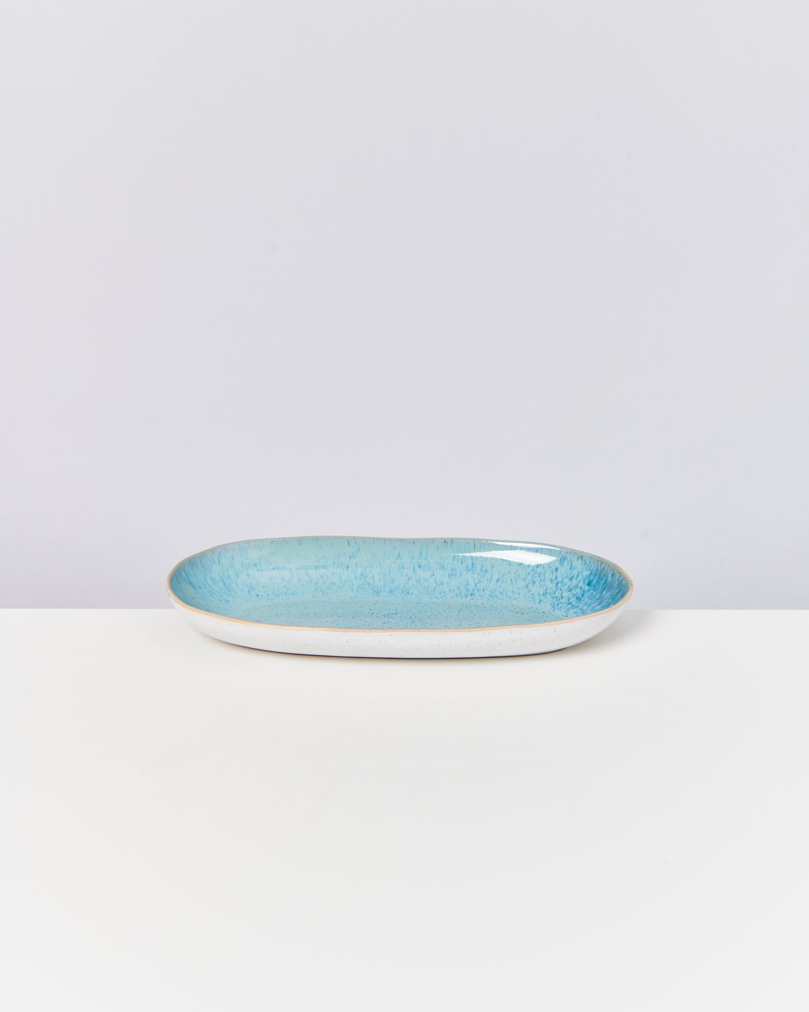 Türkisfarbener Teller mit flachem Rand auf weißem Hintergrund.