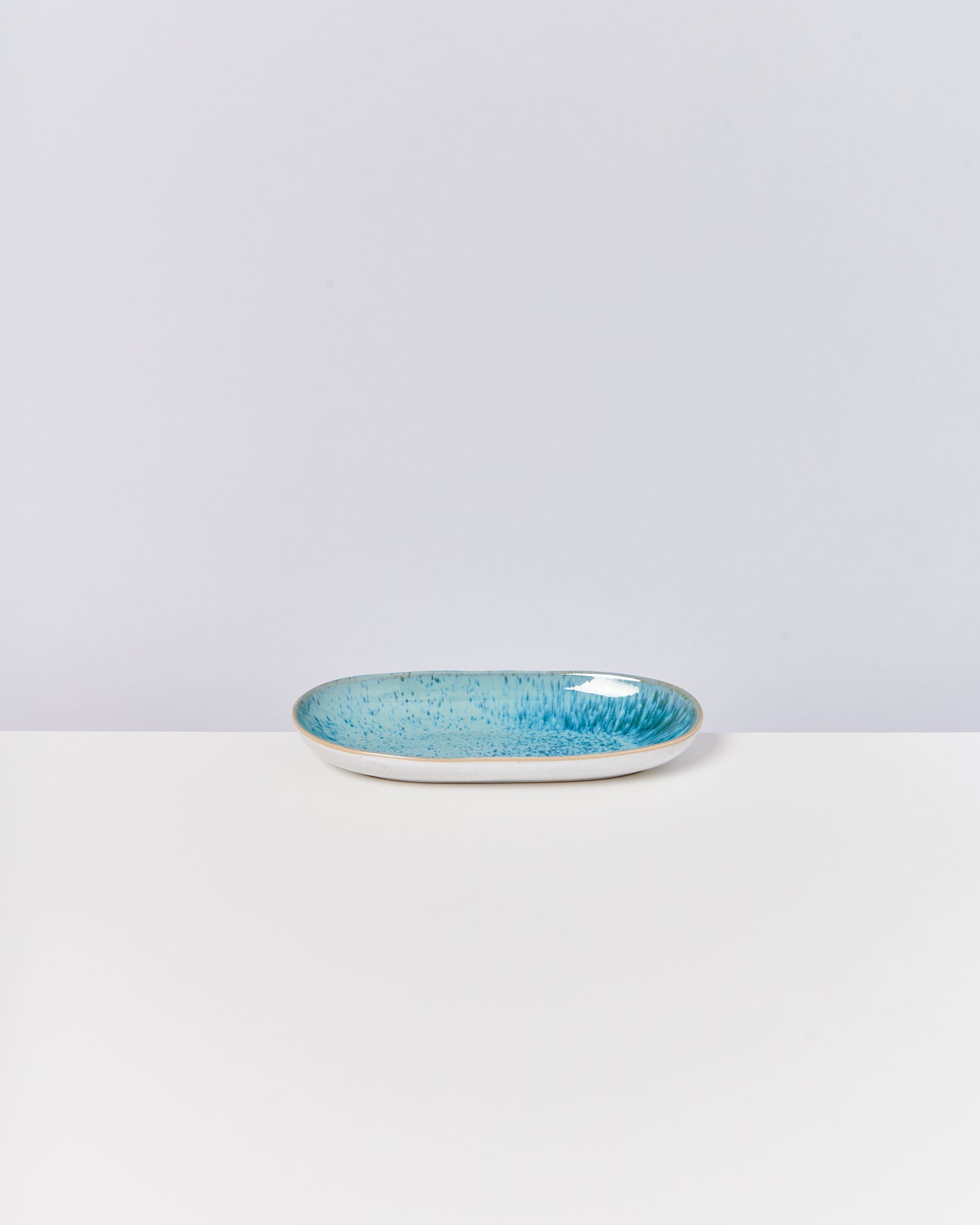 Ovale Keramikschale mit blauem, gesprenkeltem Innenbereich auf weißem Hintergrund.