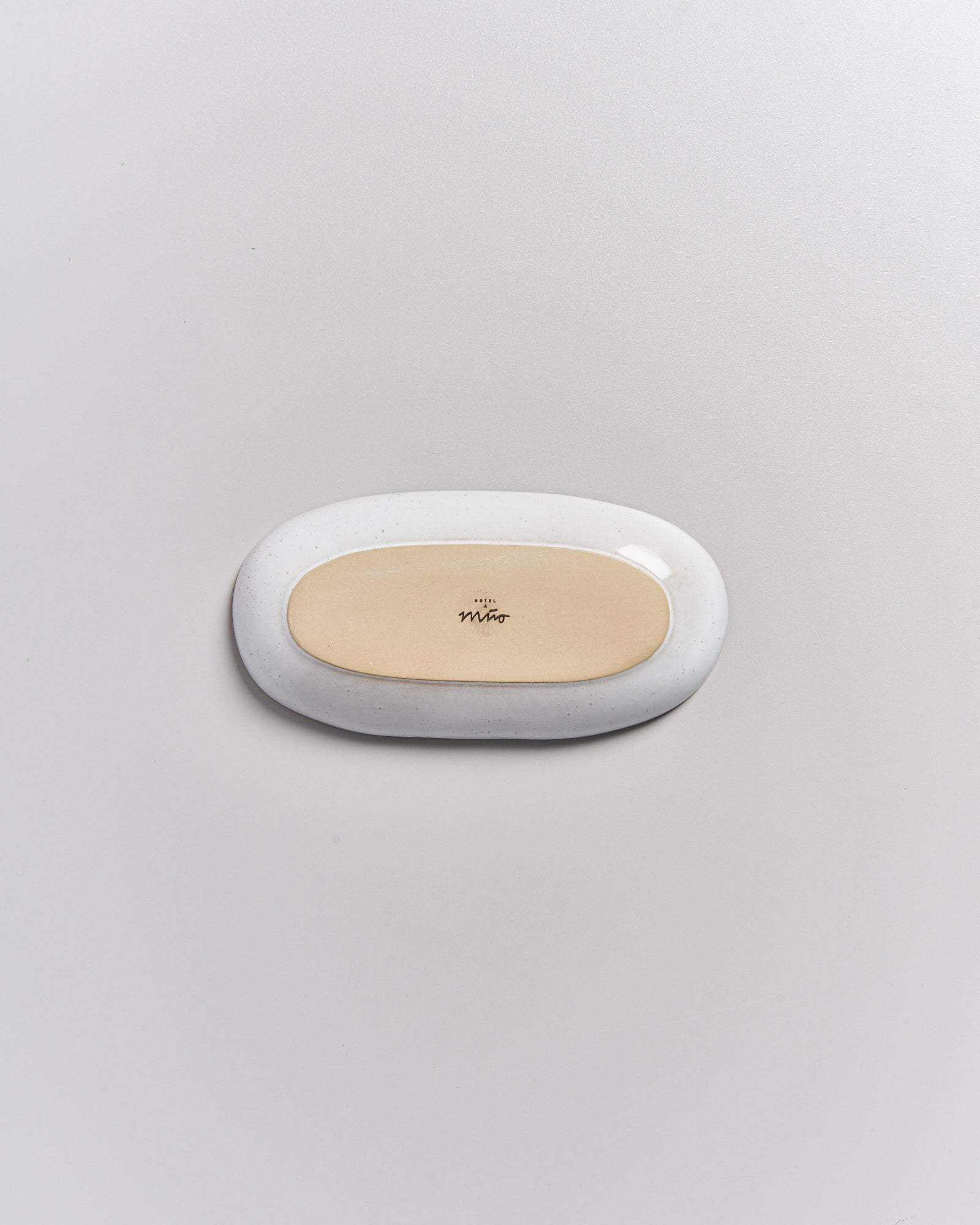 Ein ovales, bauchiges, weißes Objekt mit beiger Mitte und schwarzer Inschrift auf hellgrauem Hintergrund.