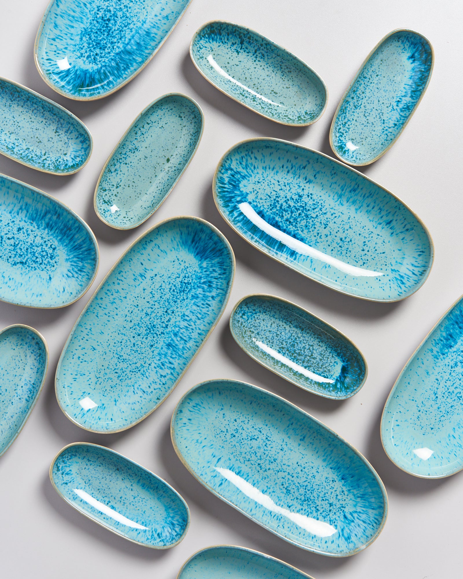 Mehrere ovale, blaue Keramikteller mit Sprenkelmuster auf weißem Hintergrund angeordnet.