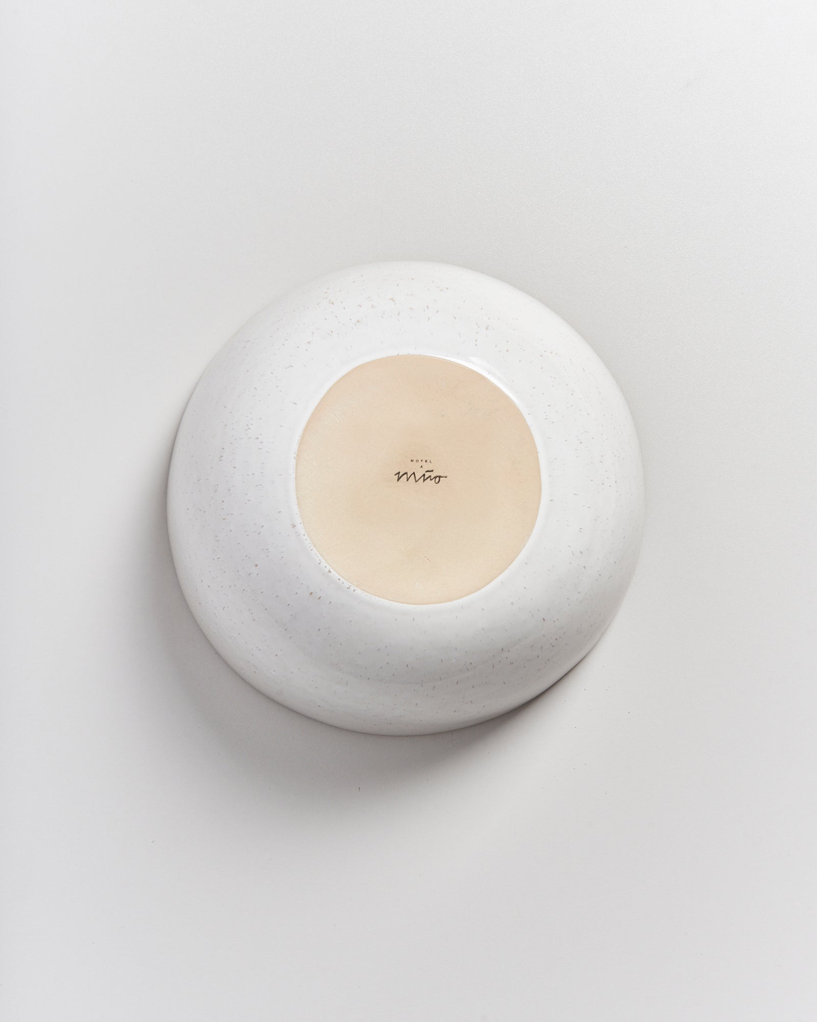 Ein umgedrehter, runder, weißer Keramikgegenstand mit einem beigefarbenen Boden und einer Unterschrift in der Mitte.