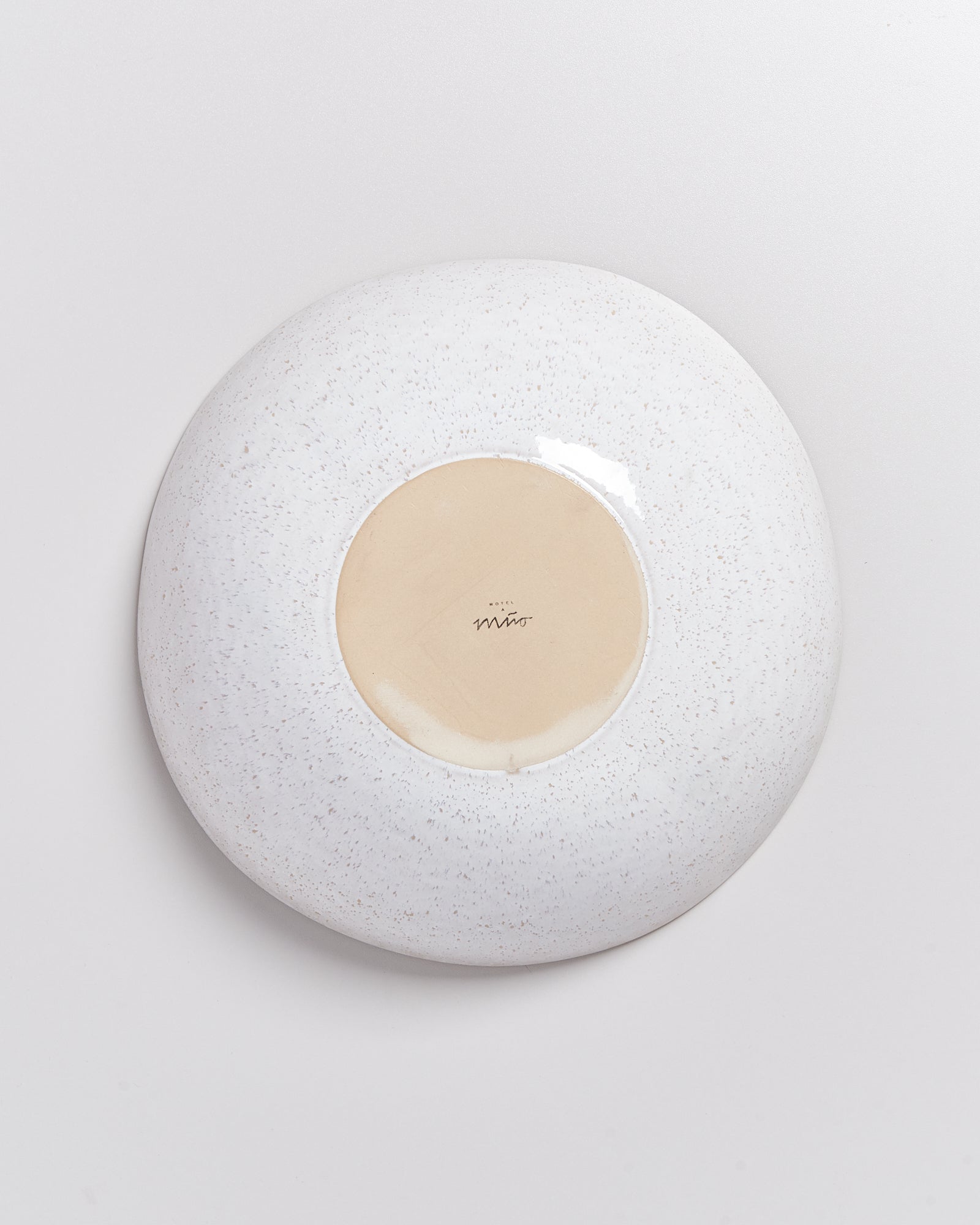 Die Unterseite eines weißen, gesprenkelten Tellers mit einem handschriftlichen Schriftzug in der Mitte.