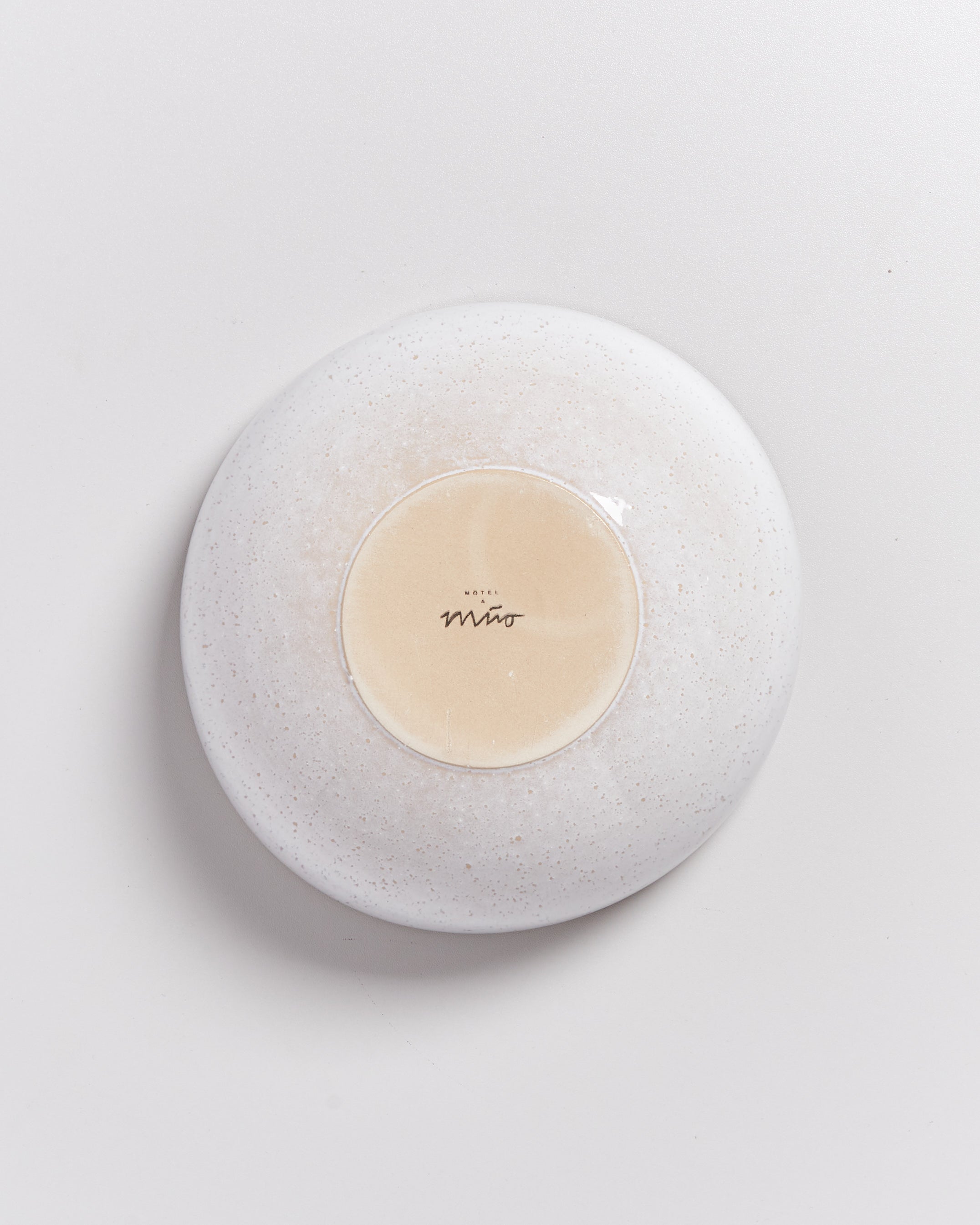 Unterseite eines keramikartigen Tellers in weißer Farbe mit einem zentralen, sandfarbenen Kreis mit der Aufschrift "Mito".