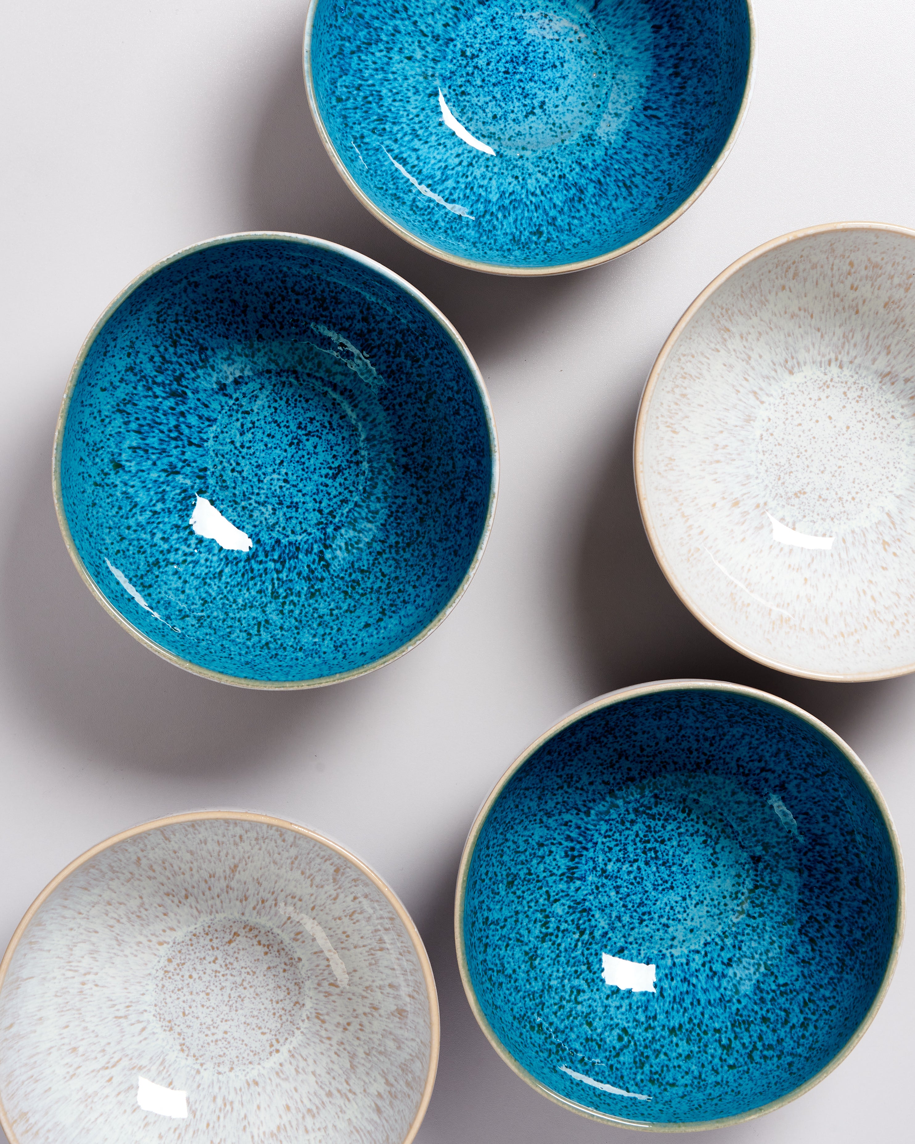 Fünf runde Schalen in Blau und Weiß mit gesprenkeltem Muster auf grauem Hintergrund.